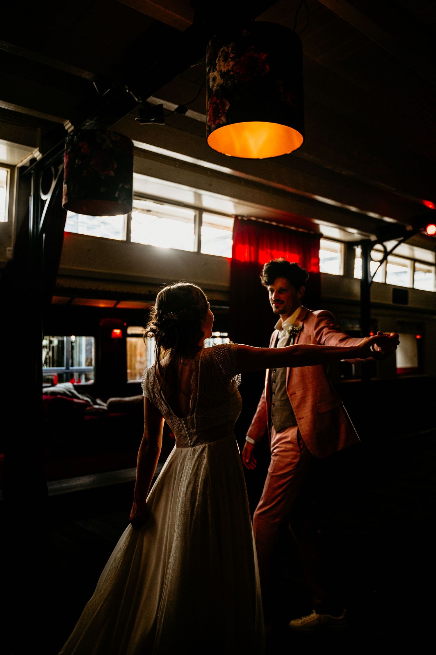 Dramatic silhouettes in dark room with orange pendant lighting.