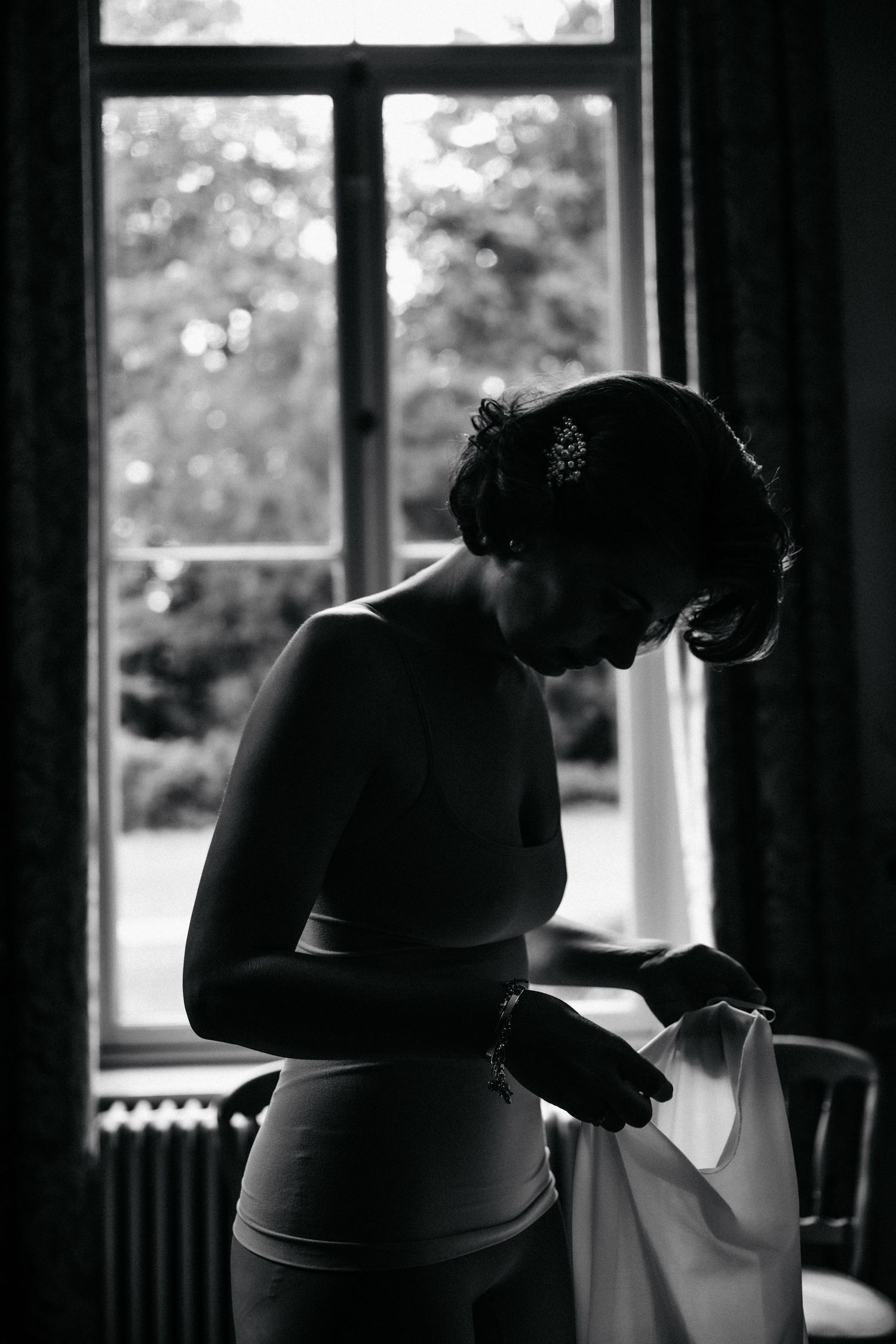 Silhouette of a person getting dressed by a window in black and white photography.