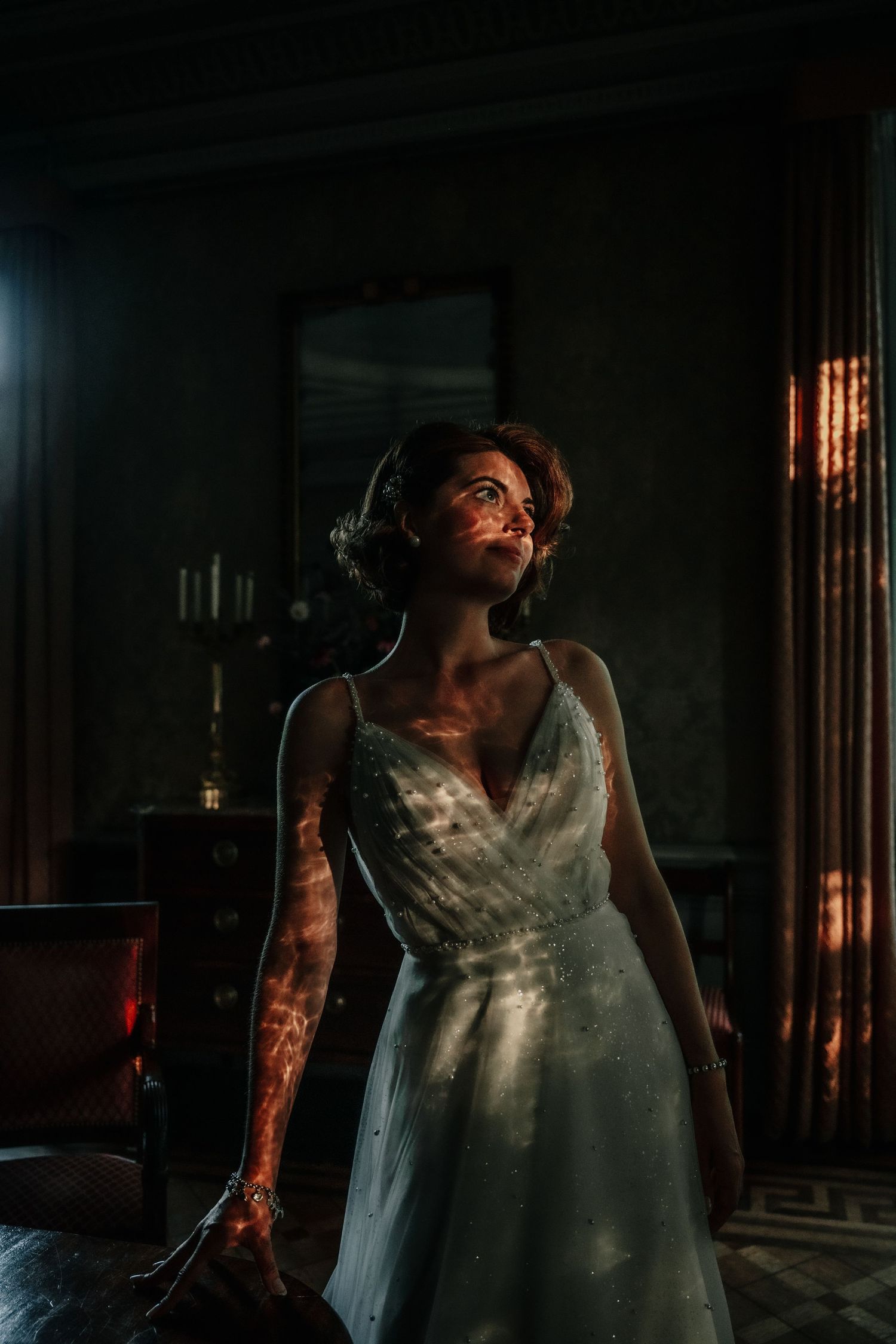 Dramatic lighting creates shadows on a white dress in a dark interior setting.