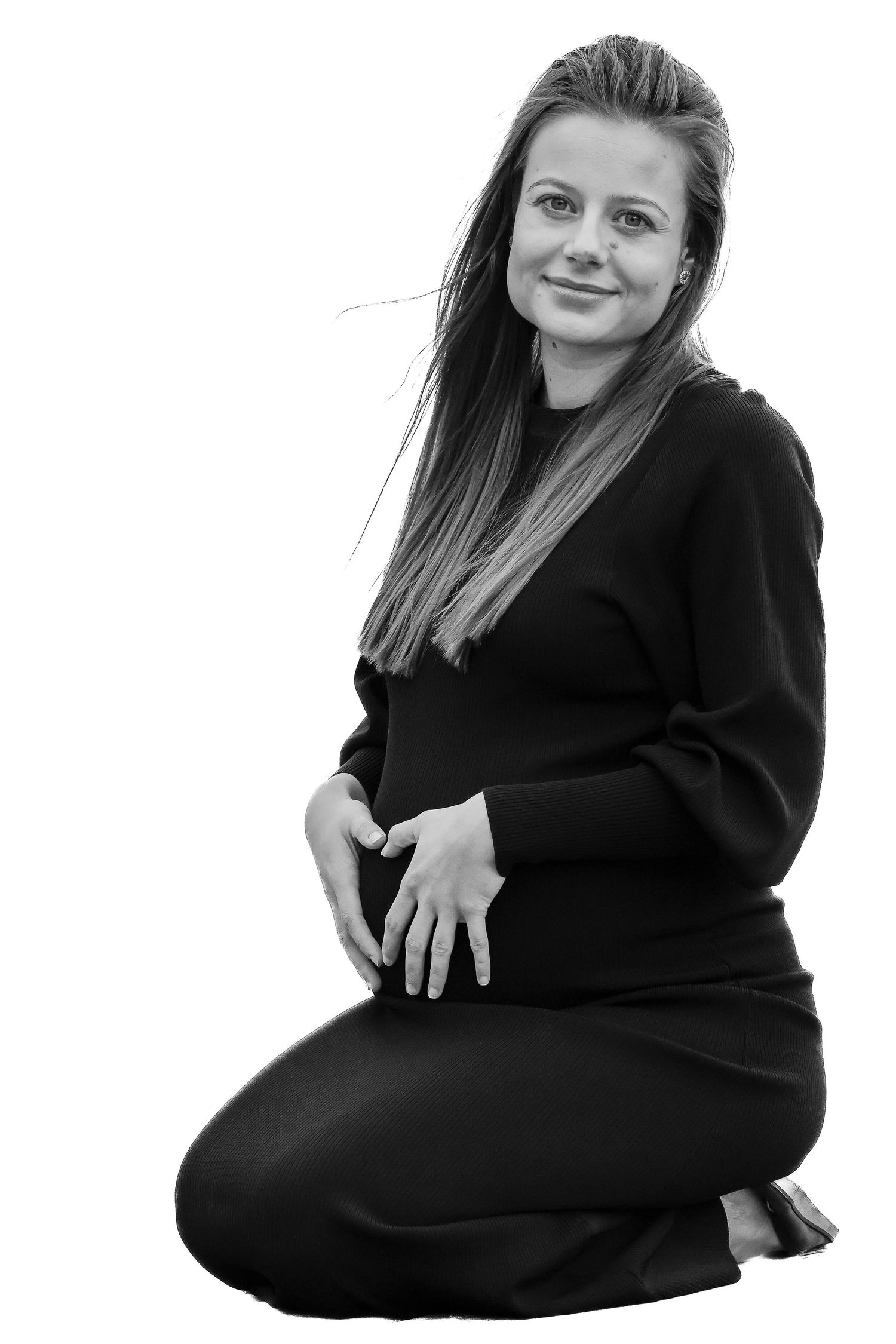 Smilende gravid kvinde sidder knælende med hænderne på maven, hvor de danner et hjerte. Et blidt og nærværende portræt. Udenfor sted og rum.