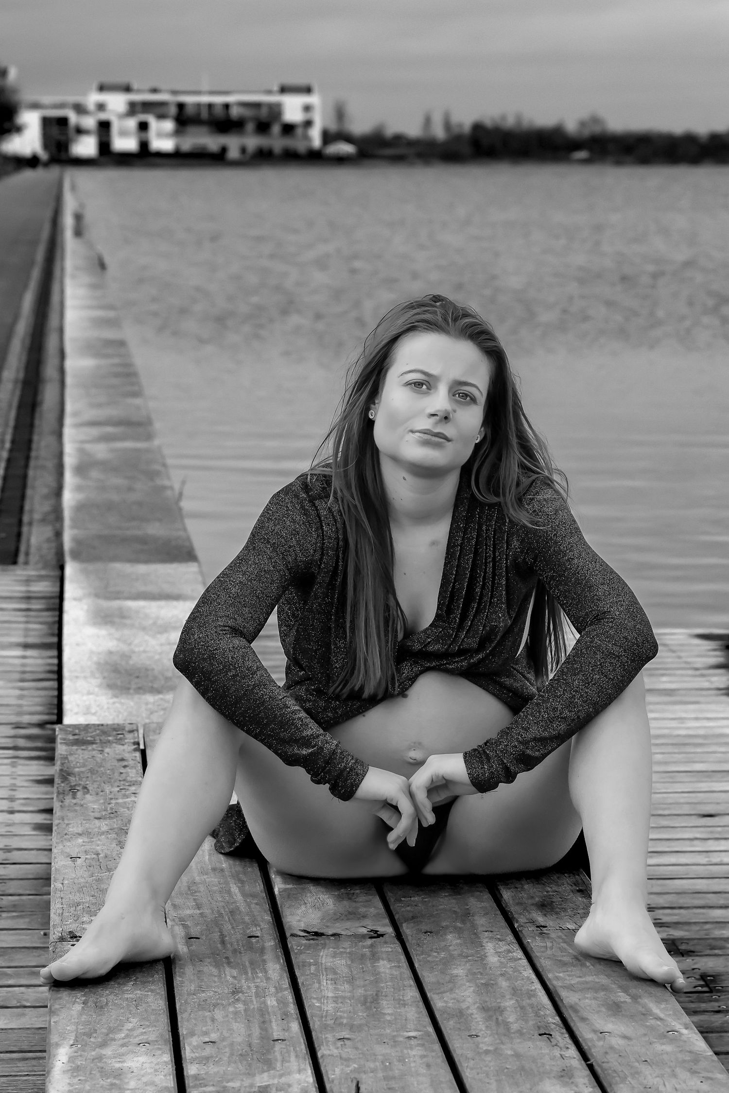 Sort/hvid kropsnært fotoportræt af gravid kvinde på overgangen mellem land og vand. Personen ser blødt mod kameraet. Åbent, ærligt og stolt.