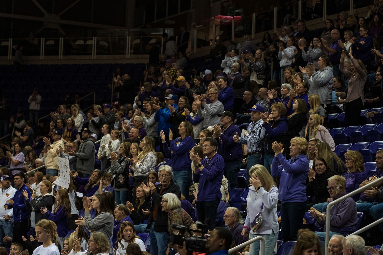 Fans in a crowded stadium stand and cheer during an exciting sporting event.