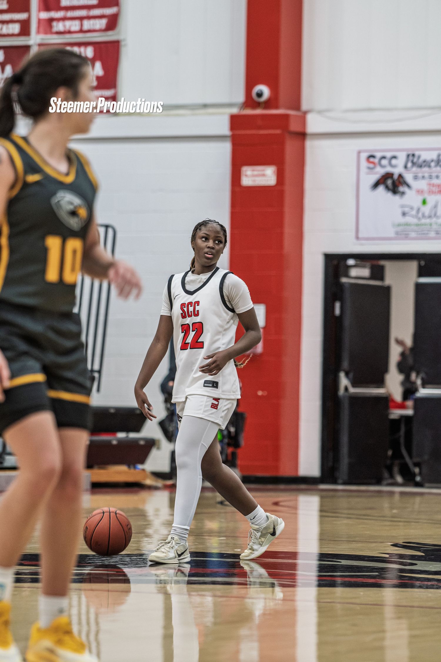 Female basketball player #22 in white SCC uniform dribbles ball during indoor college basketball game.