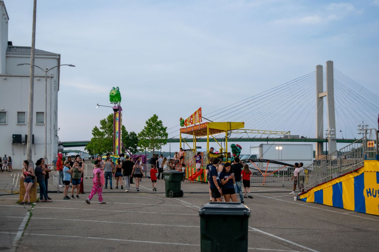 People walking along a boardwalk pier with food stands and amusement attractions visible in the distance.