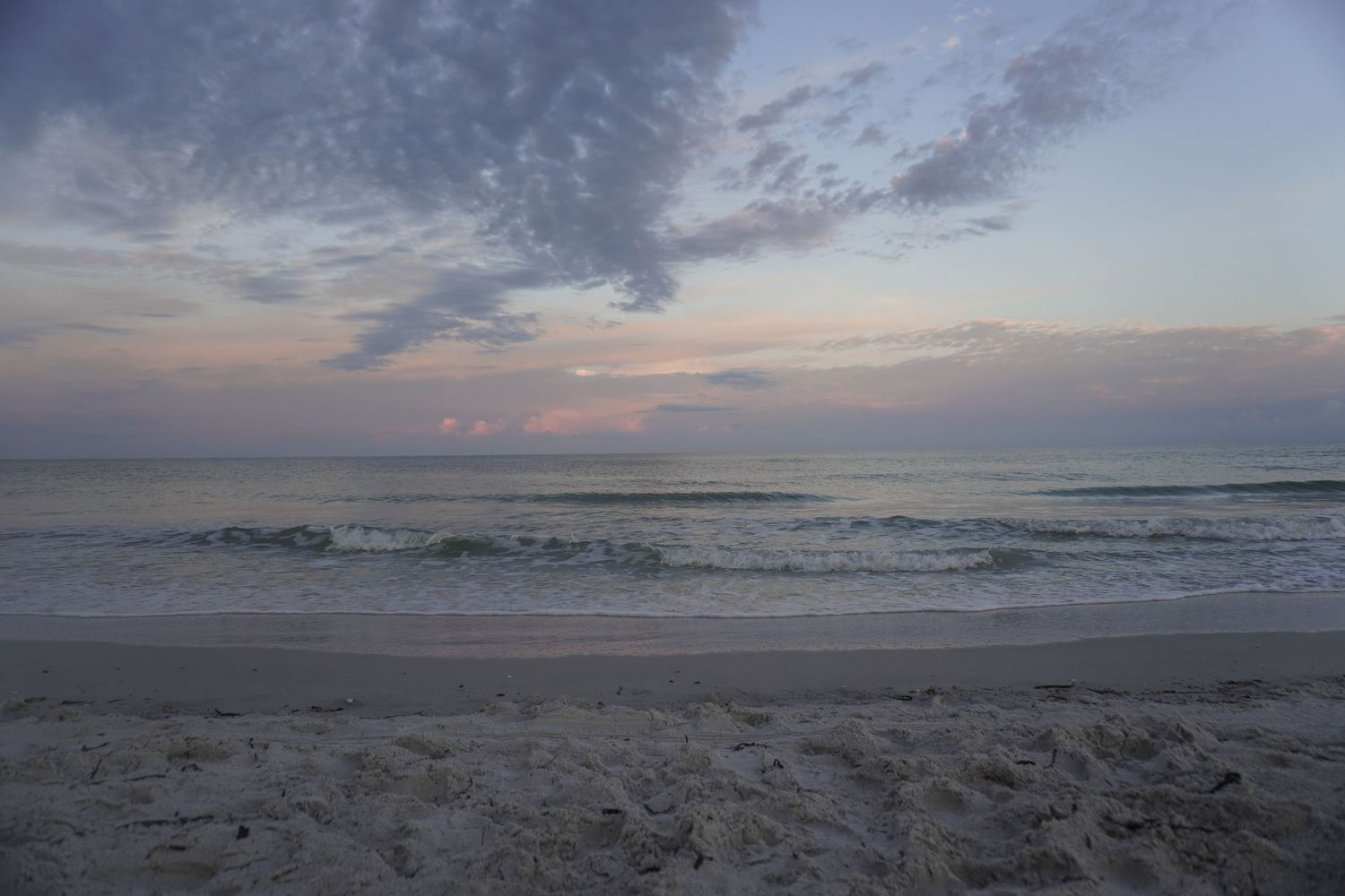 Panoramic view of empty beach at sunset with cloudy sky and calm ocean waves.