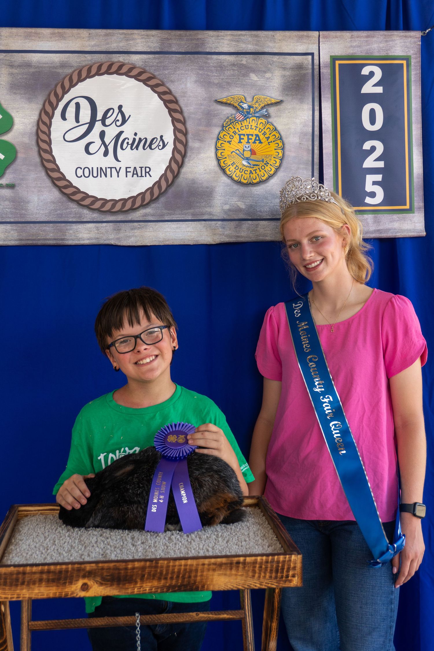 Boy with blue ribbon rabbit and fair queen at Des Moines County Fair 2025 FFA competition photo.