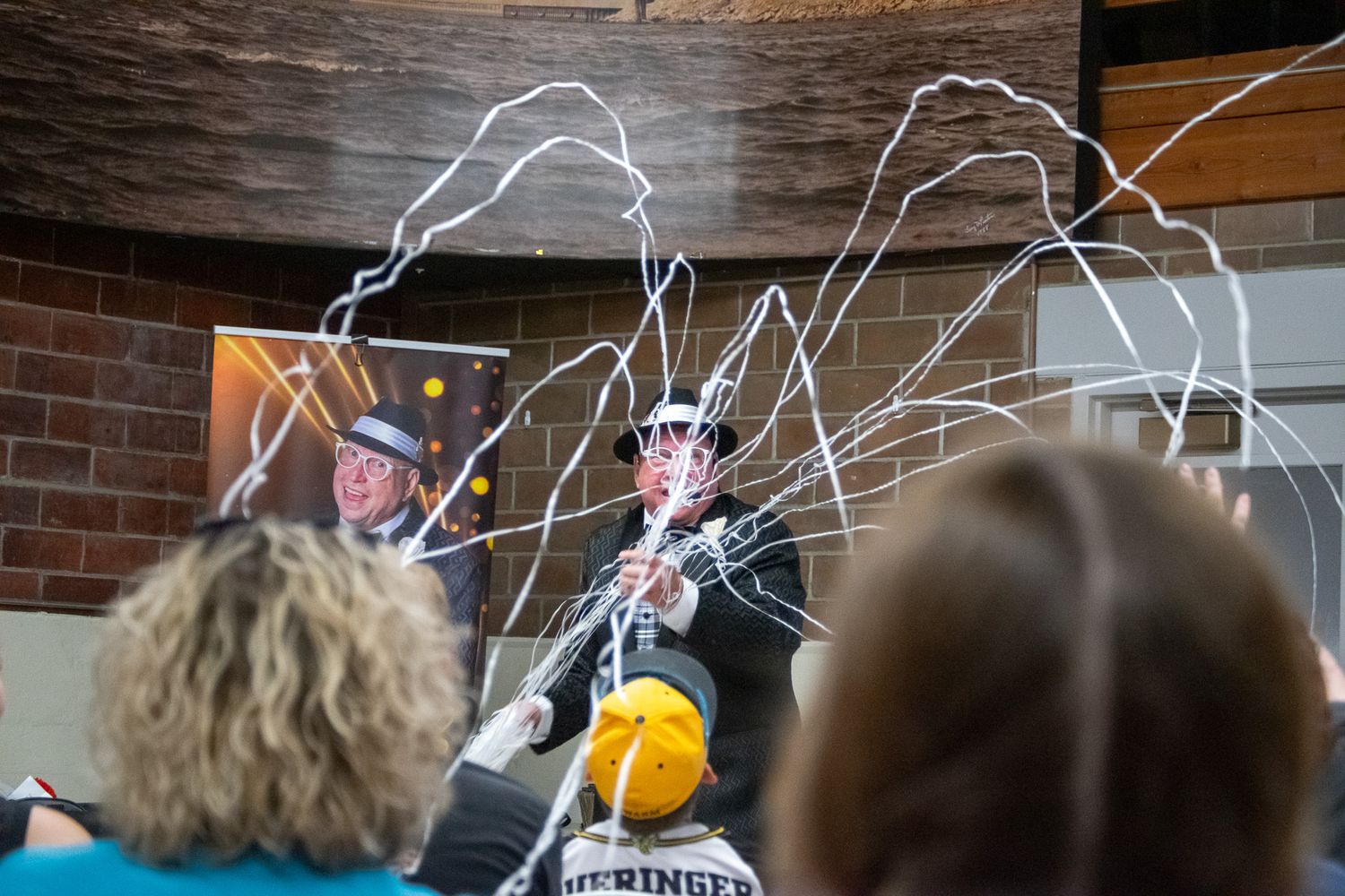 Audience watches a performer in a wizard hat create sparkling streamer effects during a live science show.