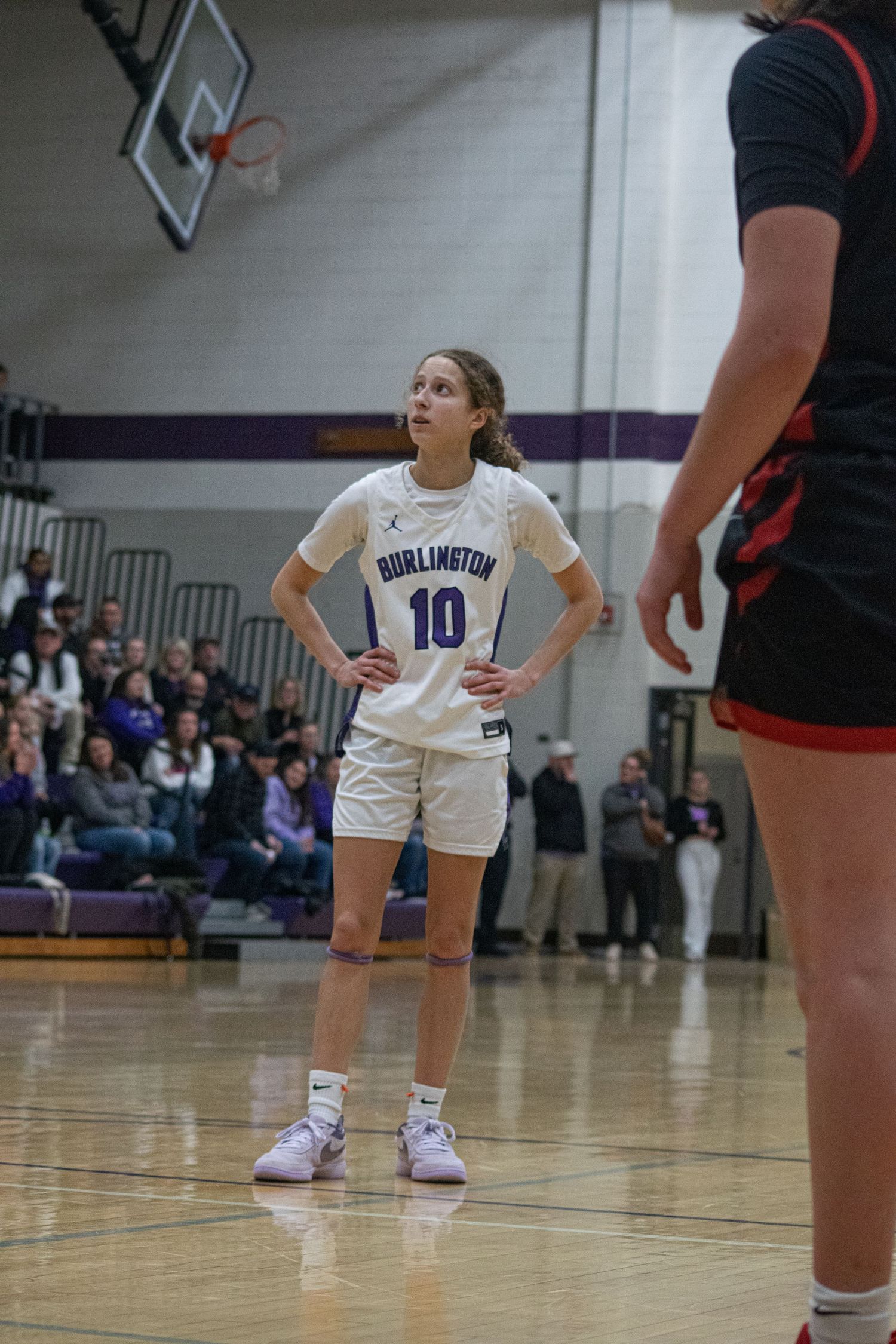 Basketball player in white uniform crouches in defensive stance during competitive game on indoor court.