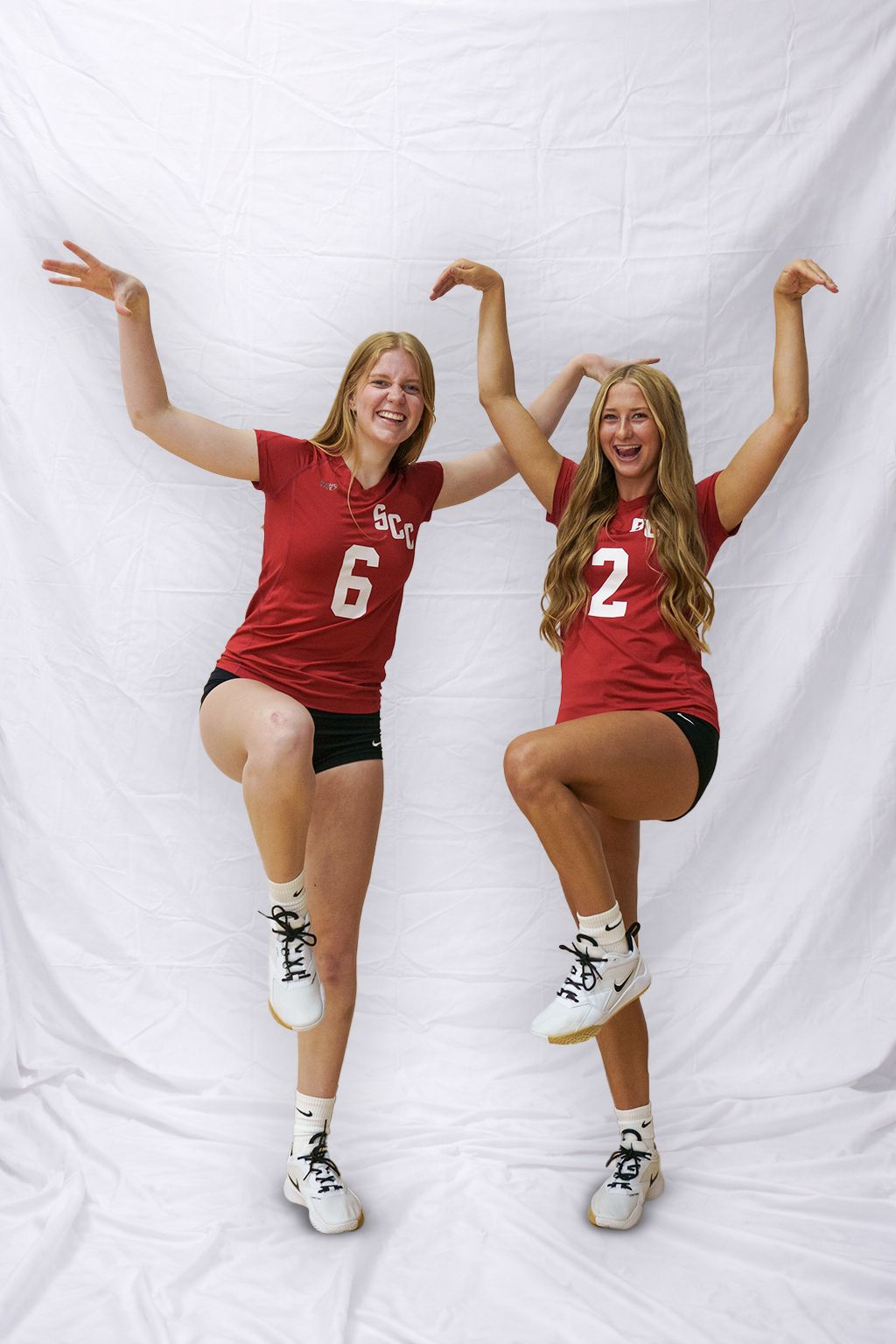 Two volleyball players in red jerseys perform dynamic jumping poses against a white backdrop.
