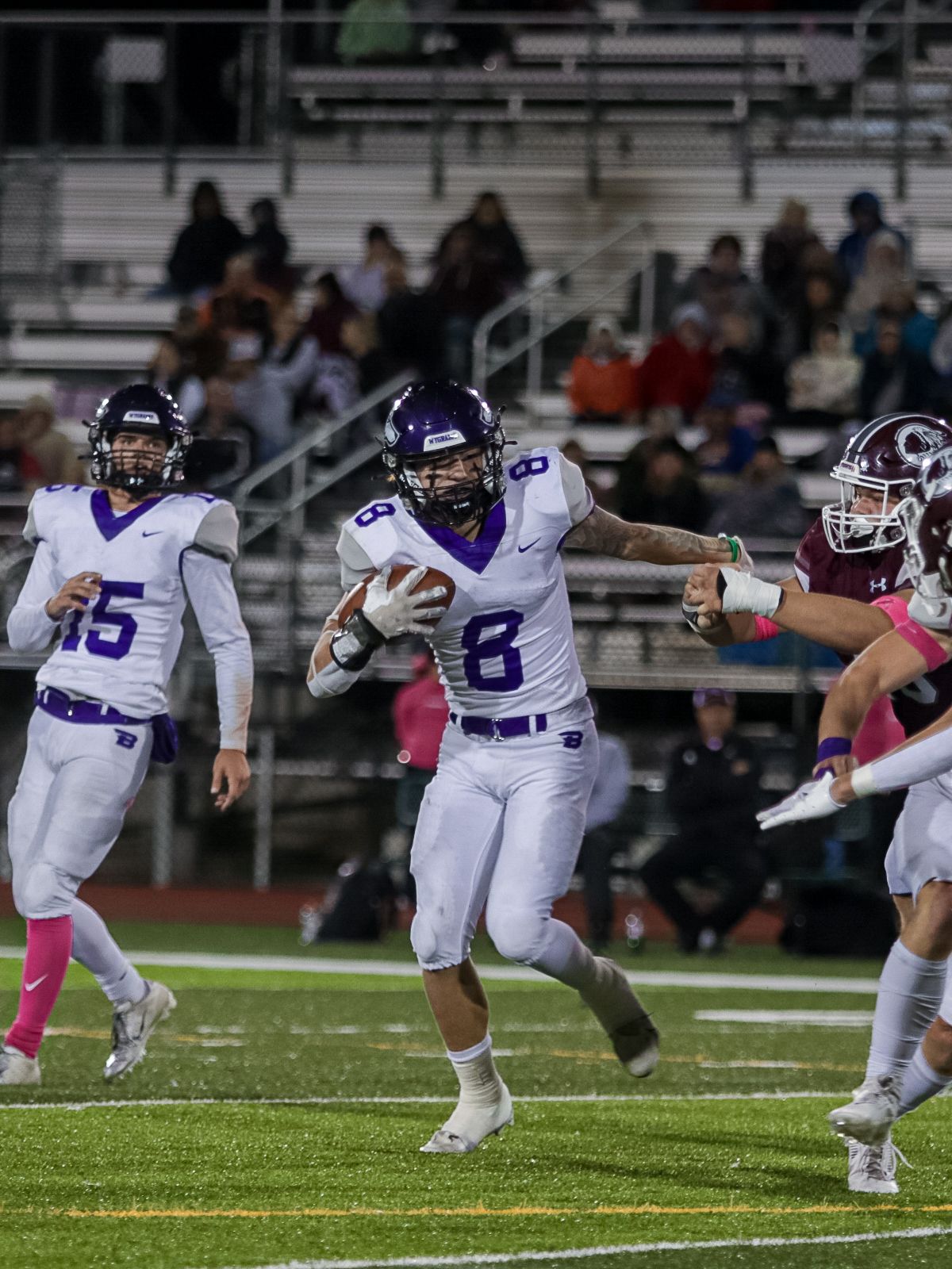 Football player in white and purple uniform diving forward on field during nighttime game.