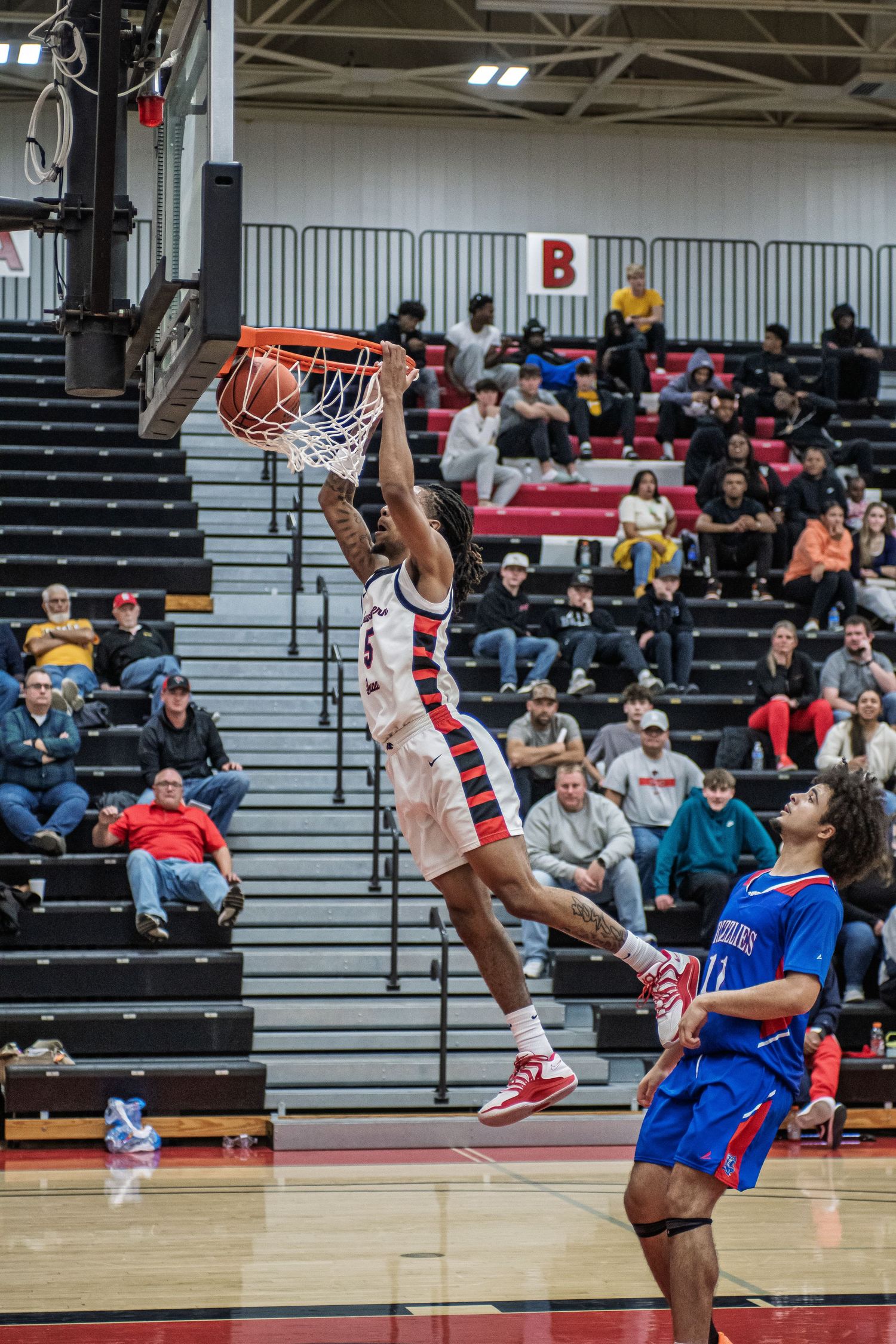 Basketball player soars through the air for an impressive slam dunk during an indoor game with spectators watching.