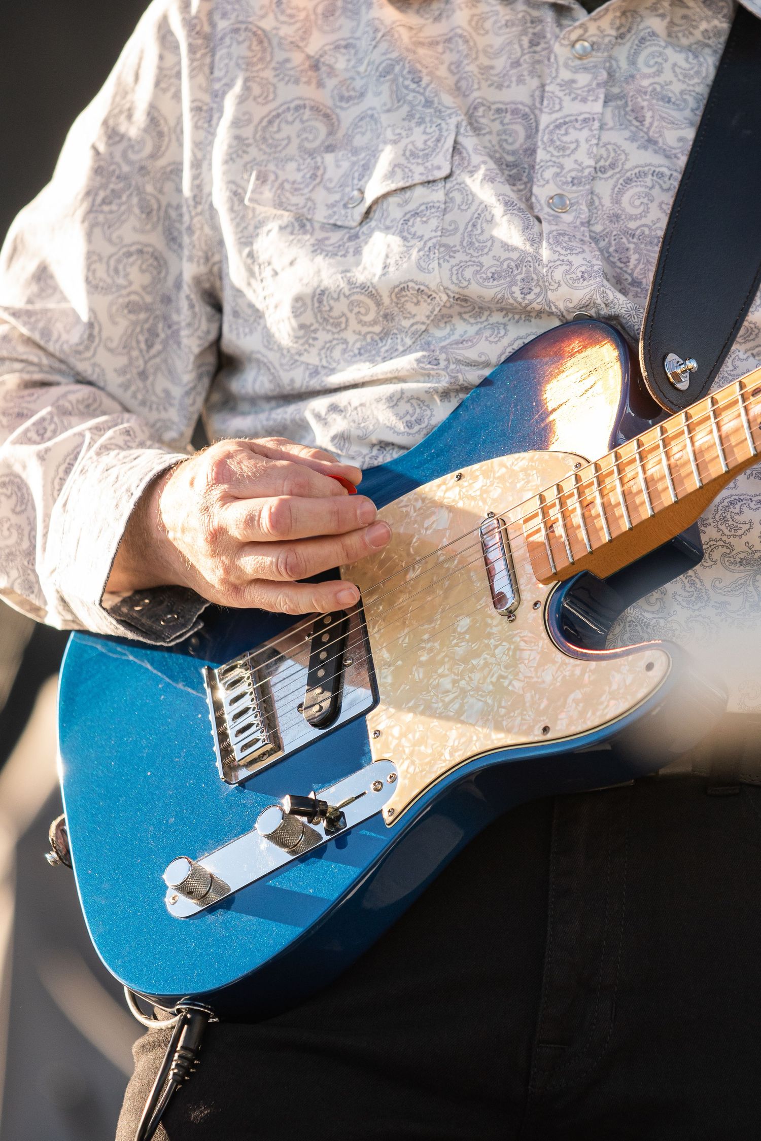 Musician playing a blue Fender Telecaster electric guitar with pearloid pickguard, wearing a paisley shirt.