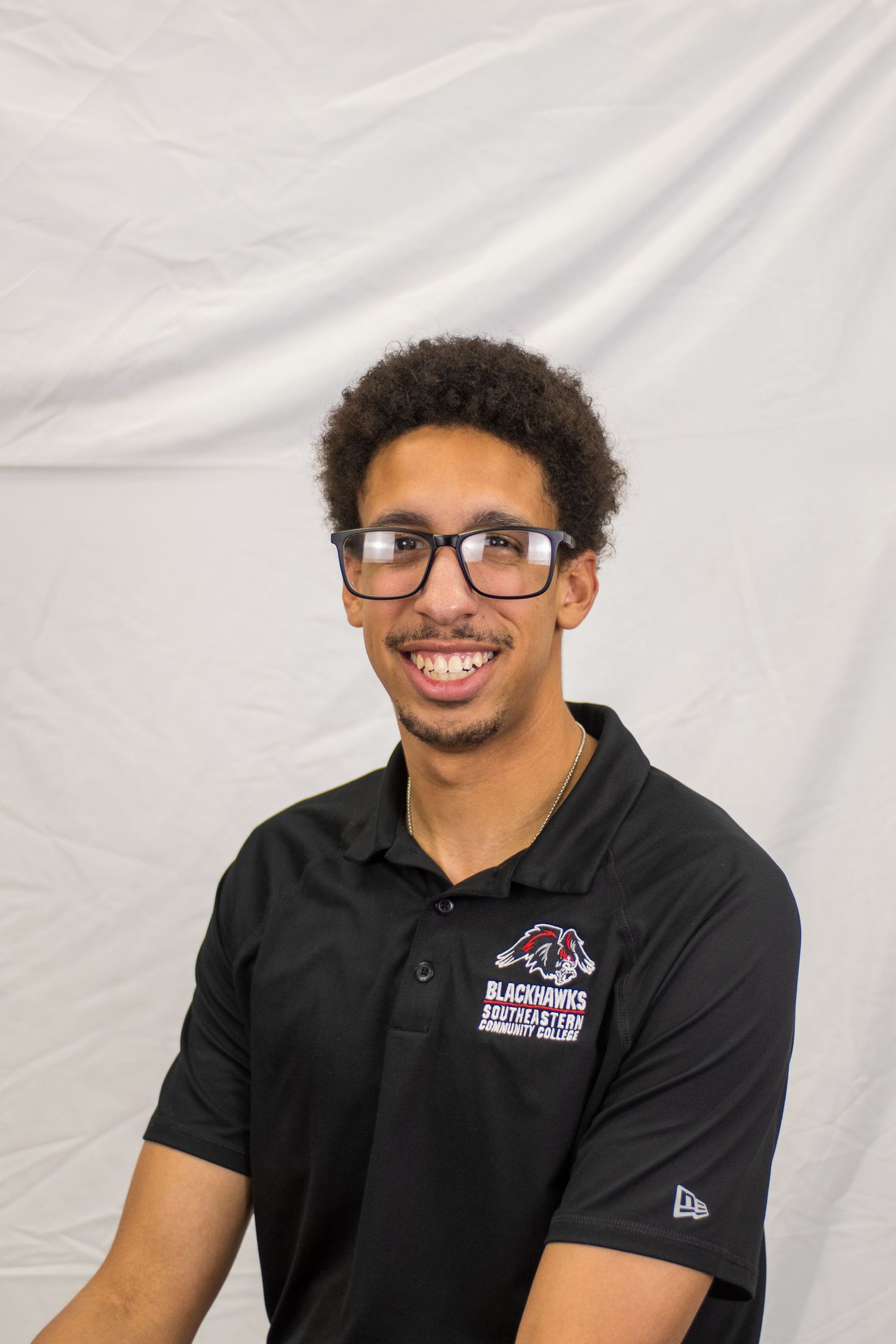 Young man in glasses and Blackhawks Southeastern Community College polo shirt smiling for a portrait photo.