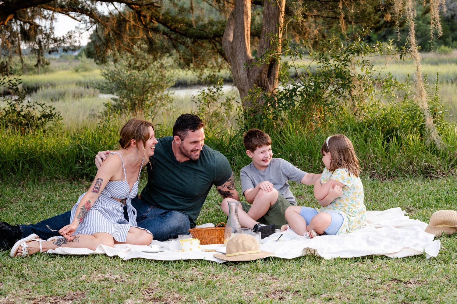 Family of four having quality time during outdoor picnic under trees.