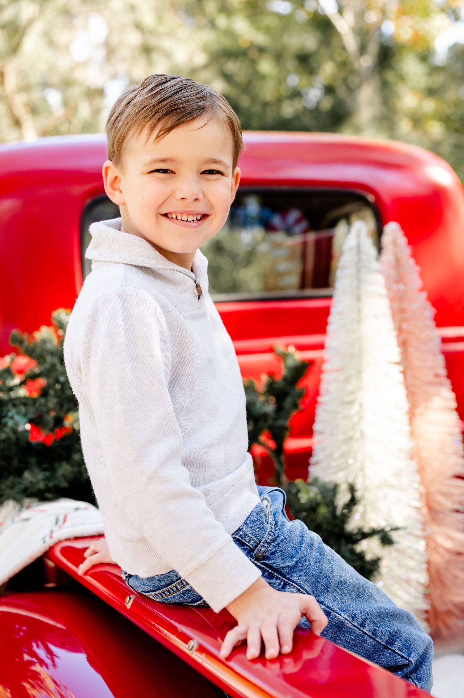 A red vintage car serves as a charming backdrop for a festive holiday photo session with white decorative trees.