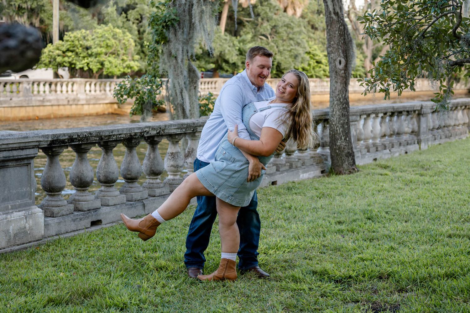 A couple shares a tender moment on a grassy lawn near a stone balustrade on a sunny afternoon at a spring mini session in jacksonville, fl.
