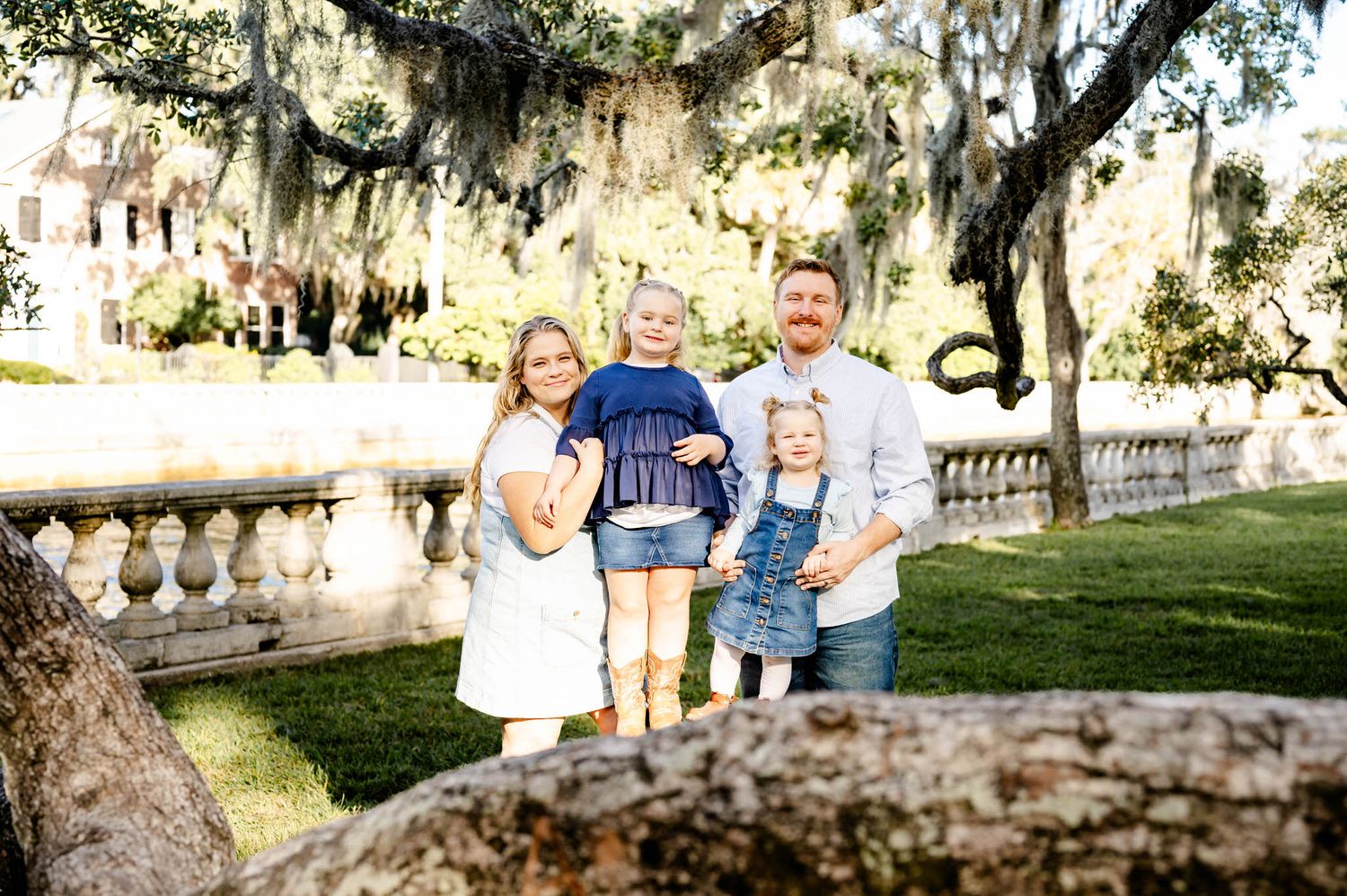 Family enjoying a sunny afternoon in a park with Spanish moss hanging from trees in the background.