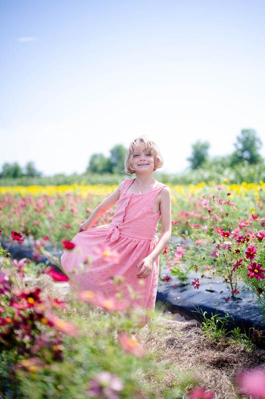 Little girl facing the camera and smiling at a flower field during a family spring mini photo session at Brandford Farm in Jacksonville FL