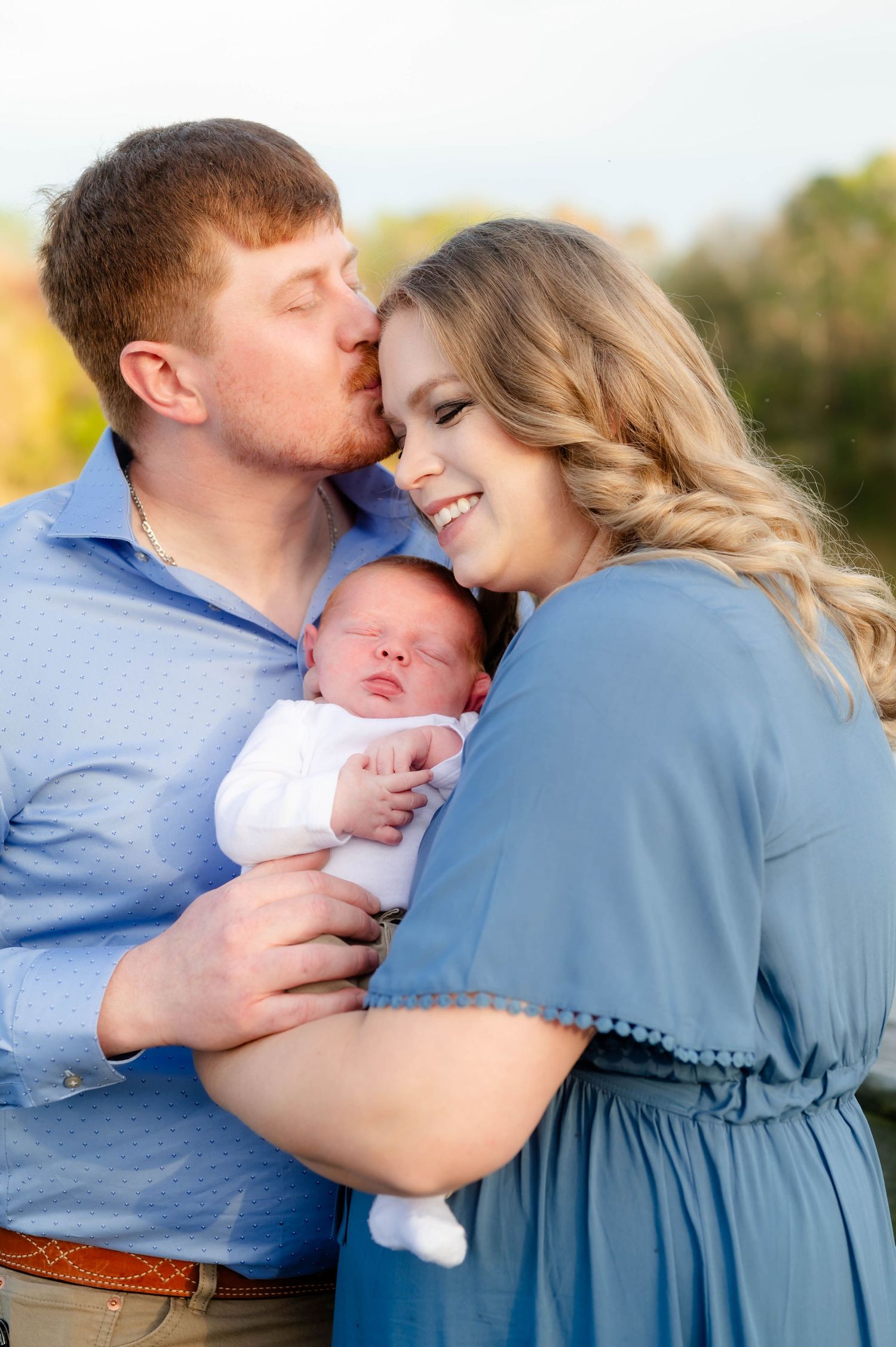 Parents sharing intimate moment with newborn baby outdoors during family photoshoot.