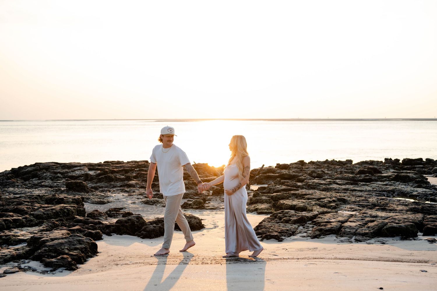 Couple walking hand in hand along rocky coastline during sunset.
