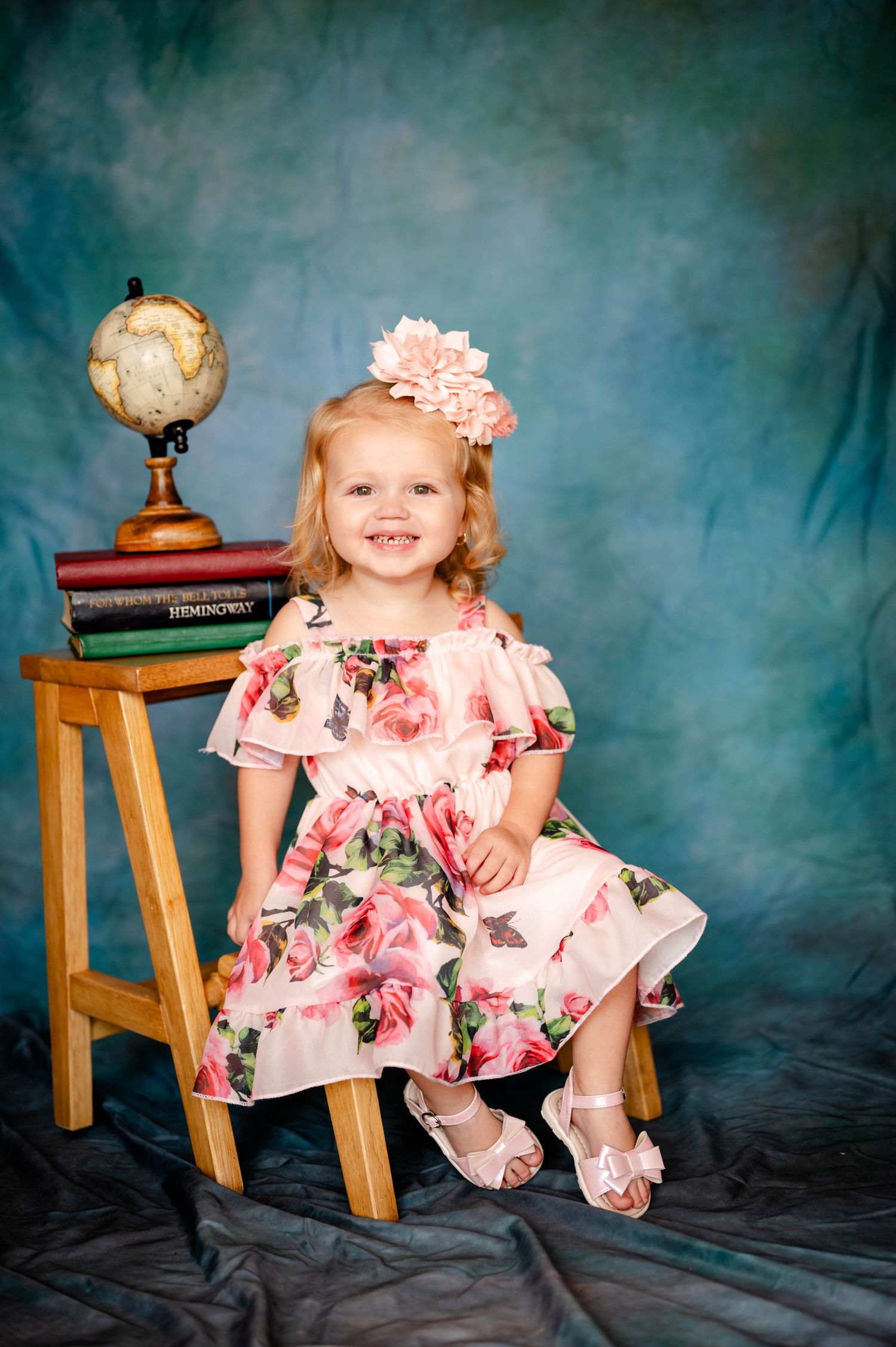 Child in floral dress sitting near wooden stool with pumpkin decoration in her Jacksonville preschool photo session.
