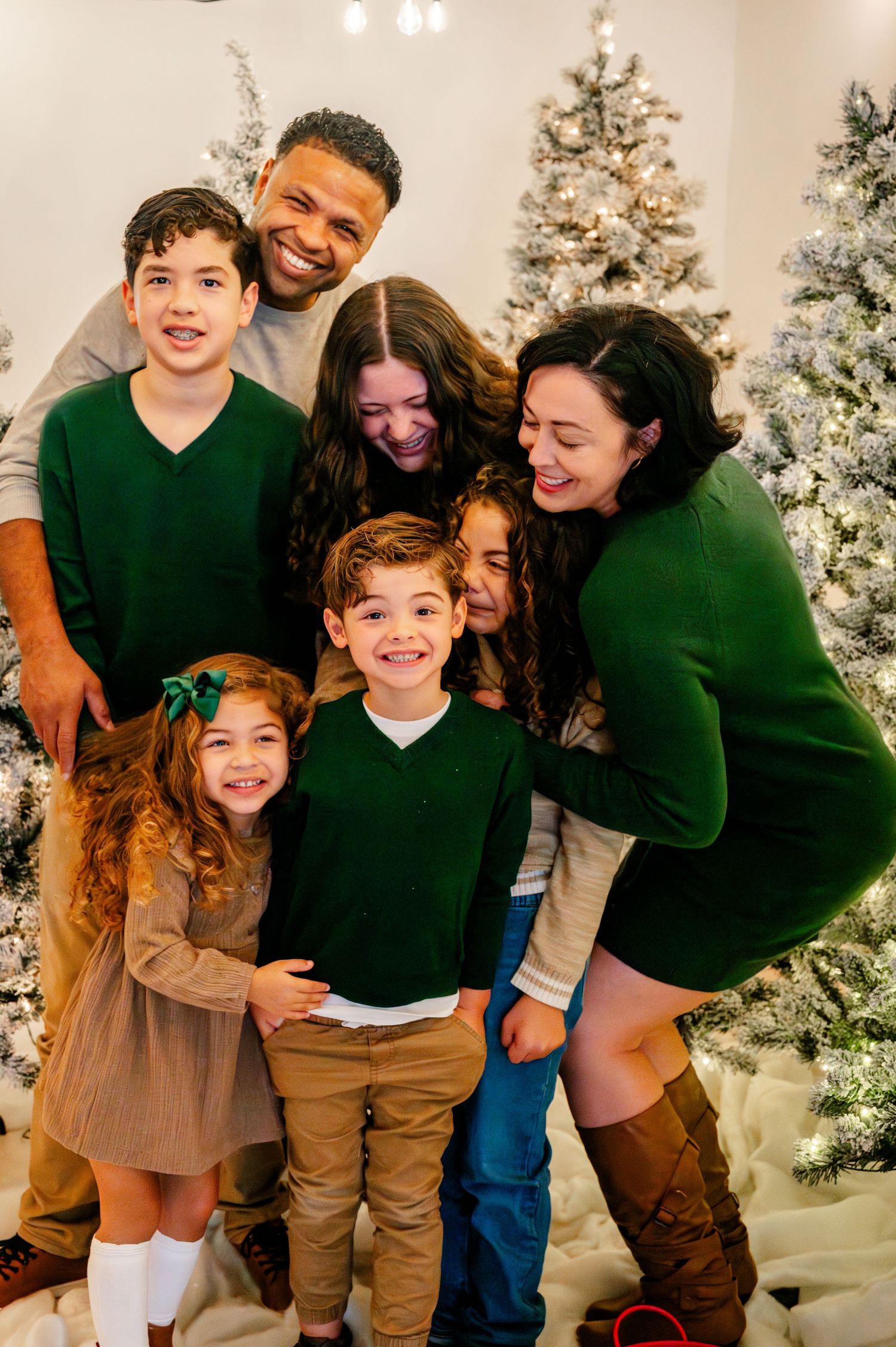 A family poses together in matching outfits in front of decorated white Christmas trees for holiday photos.