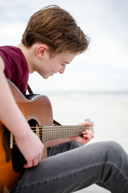 High school senior playing guitar at a Jacksonville FL beach during his senior photoshoot
