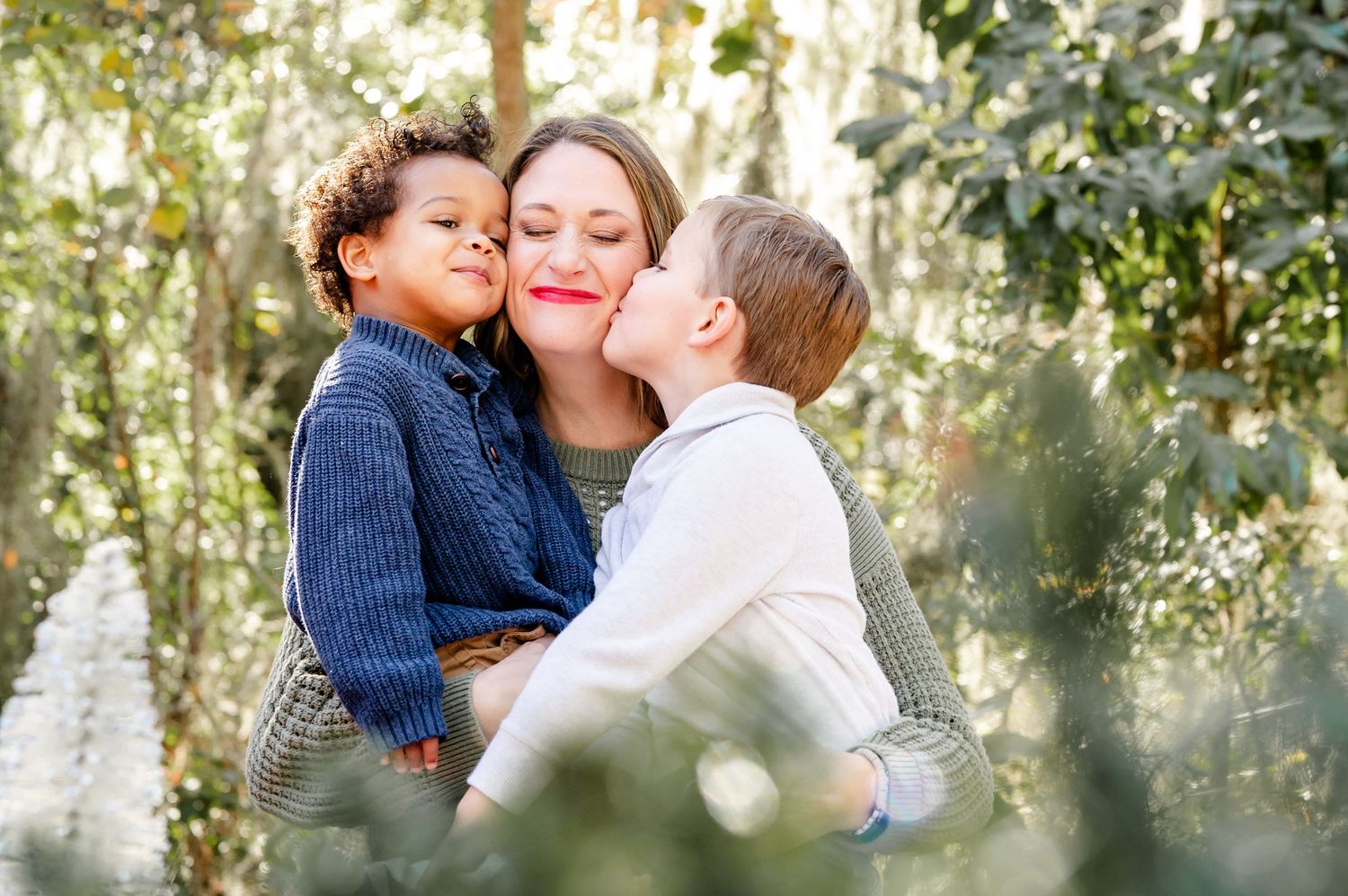 Tender family moment captured in a sunlit garden setting with natural bokeh effect in the background.