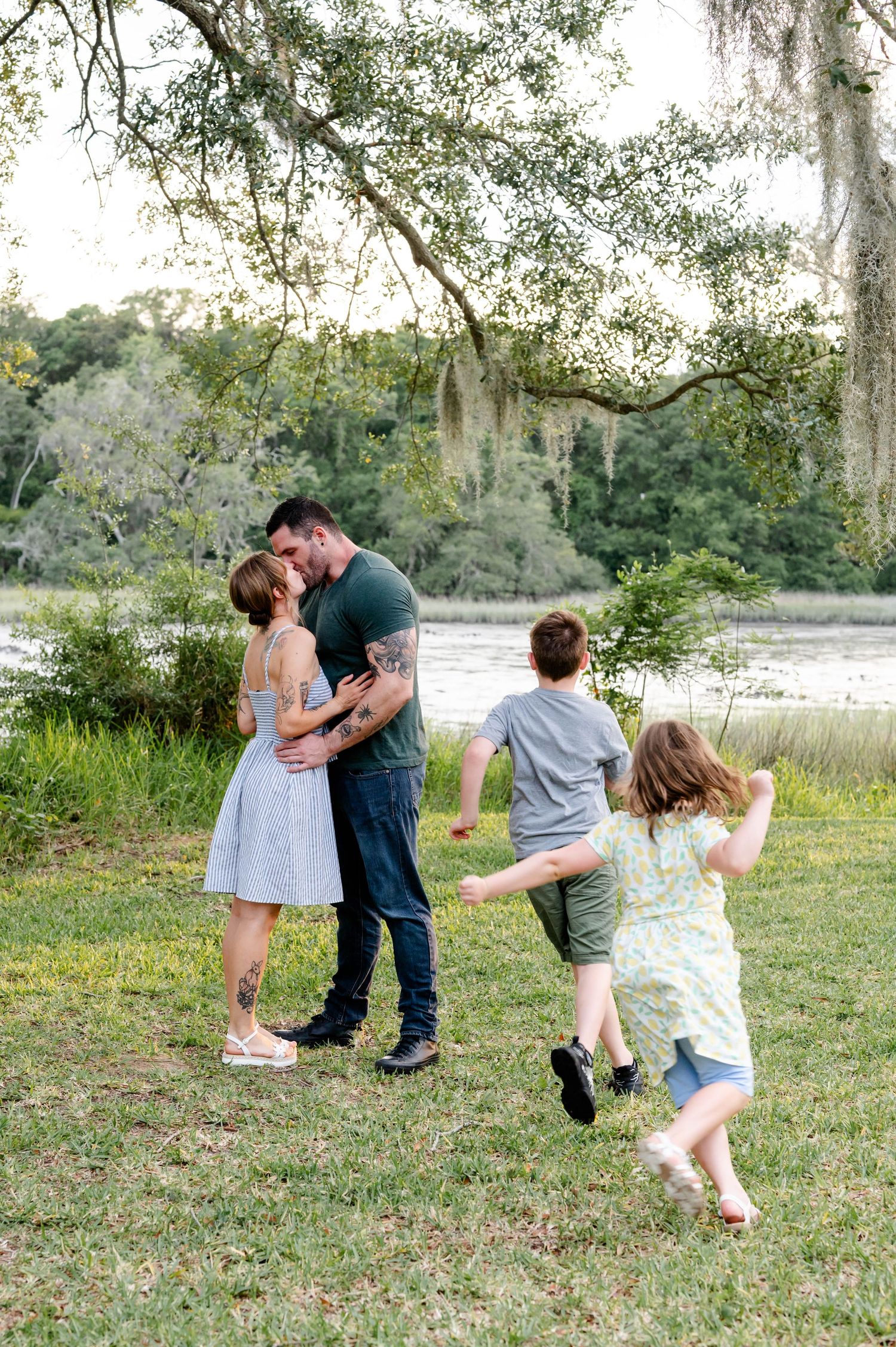 A family spending time together outdoors near a lake with children playing in the background.