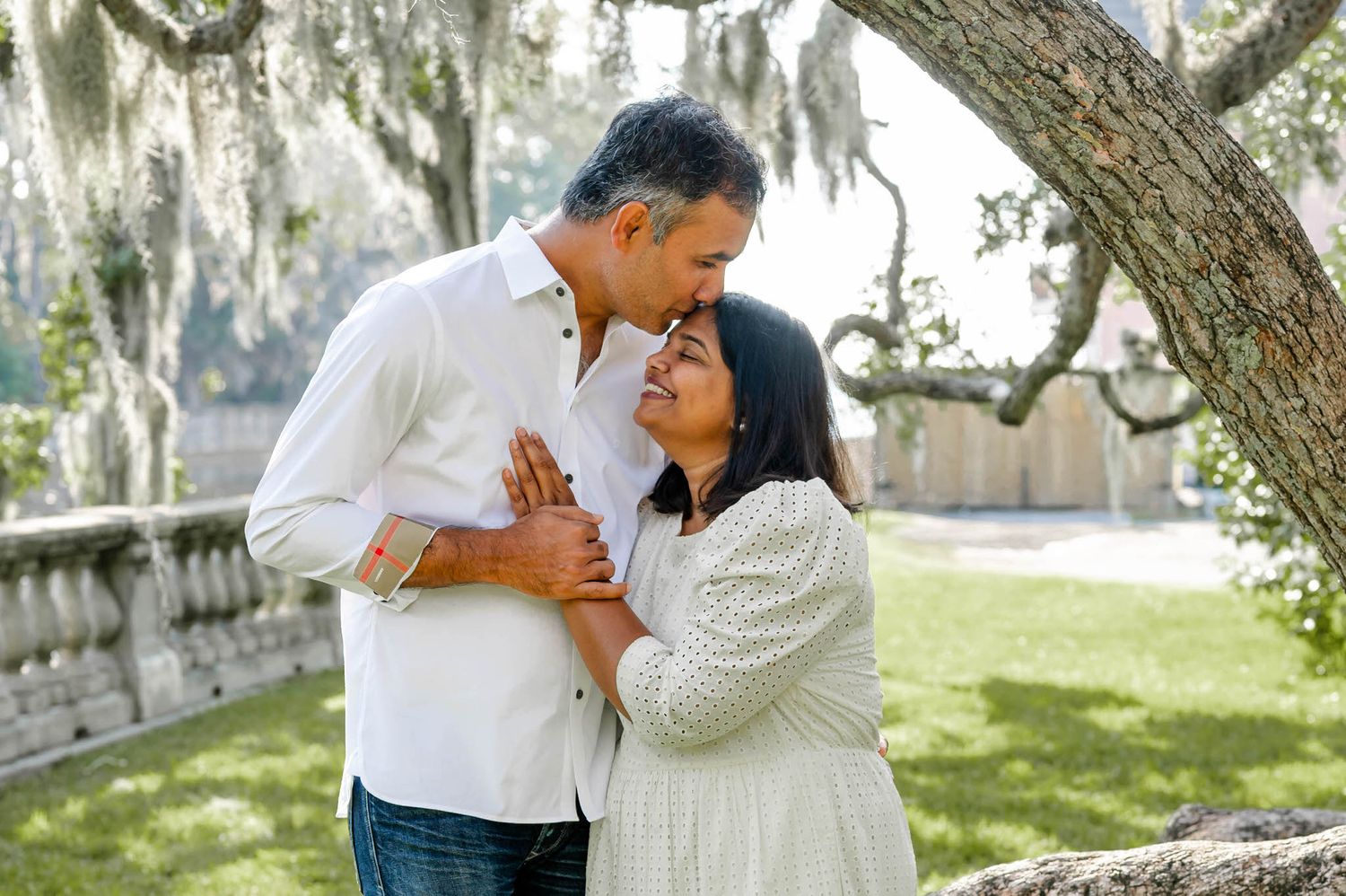 Romantic couple shares tender moments under Spanish moss draped oak trees in a sunlit garden at a spring mini session in jacksonville, fl.