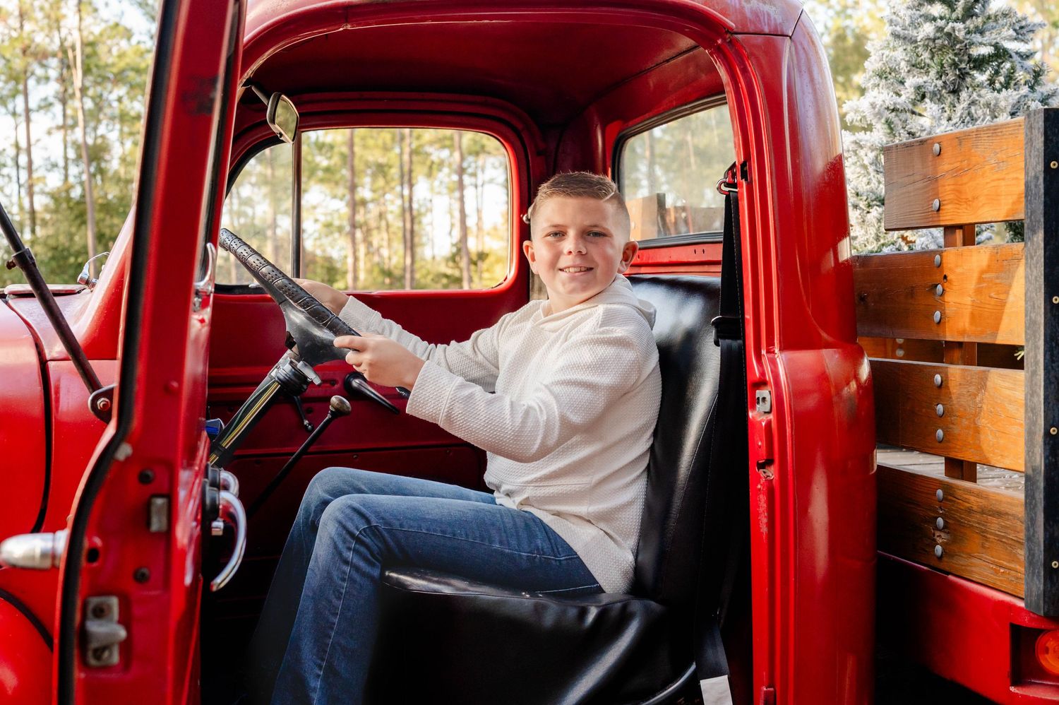 Young boy sits in the driver's seat of a vintage red pickup truck with wooden sideboards at a Christmas mini session in Jacksonville, FL.