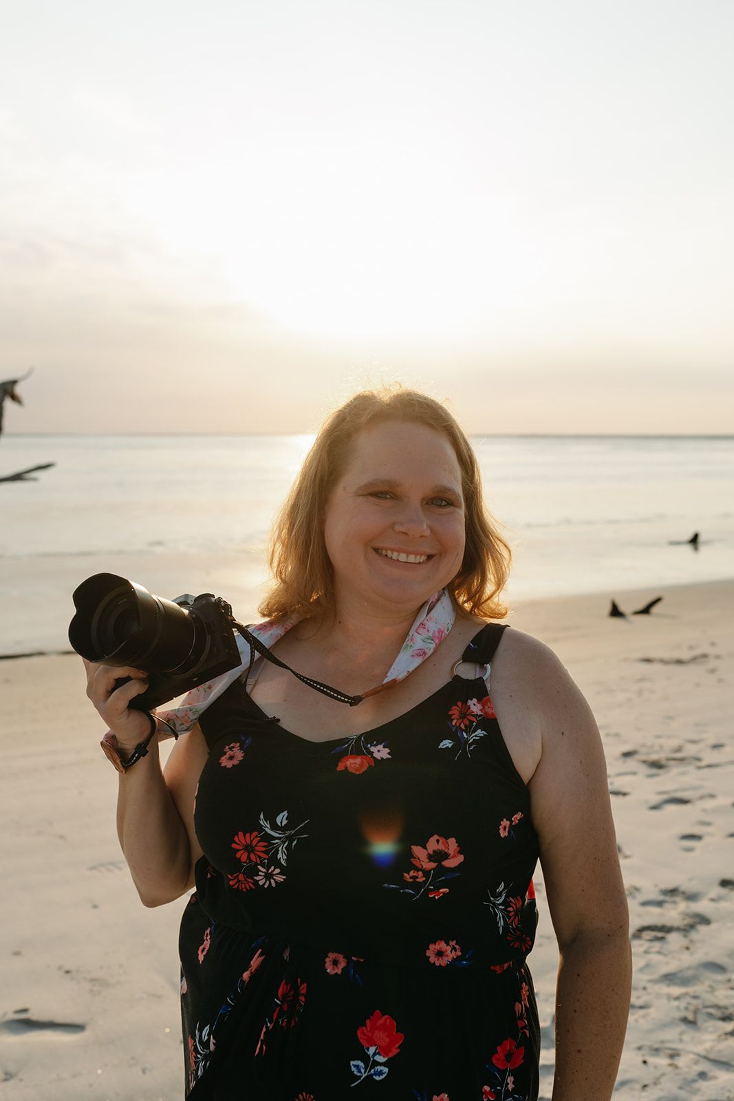 Jacksonville Family Photographer Jessica Life wearing floral dress captures sunset photos on sandy beach.