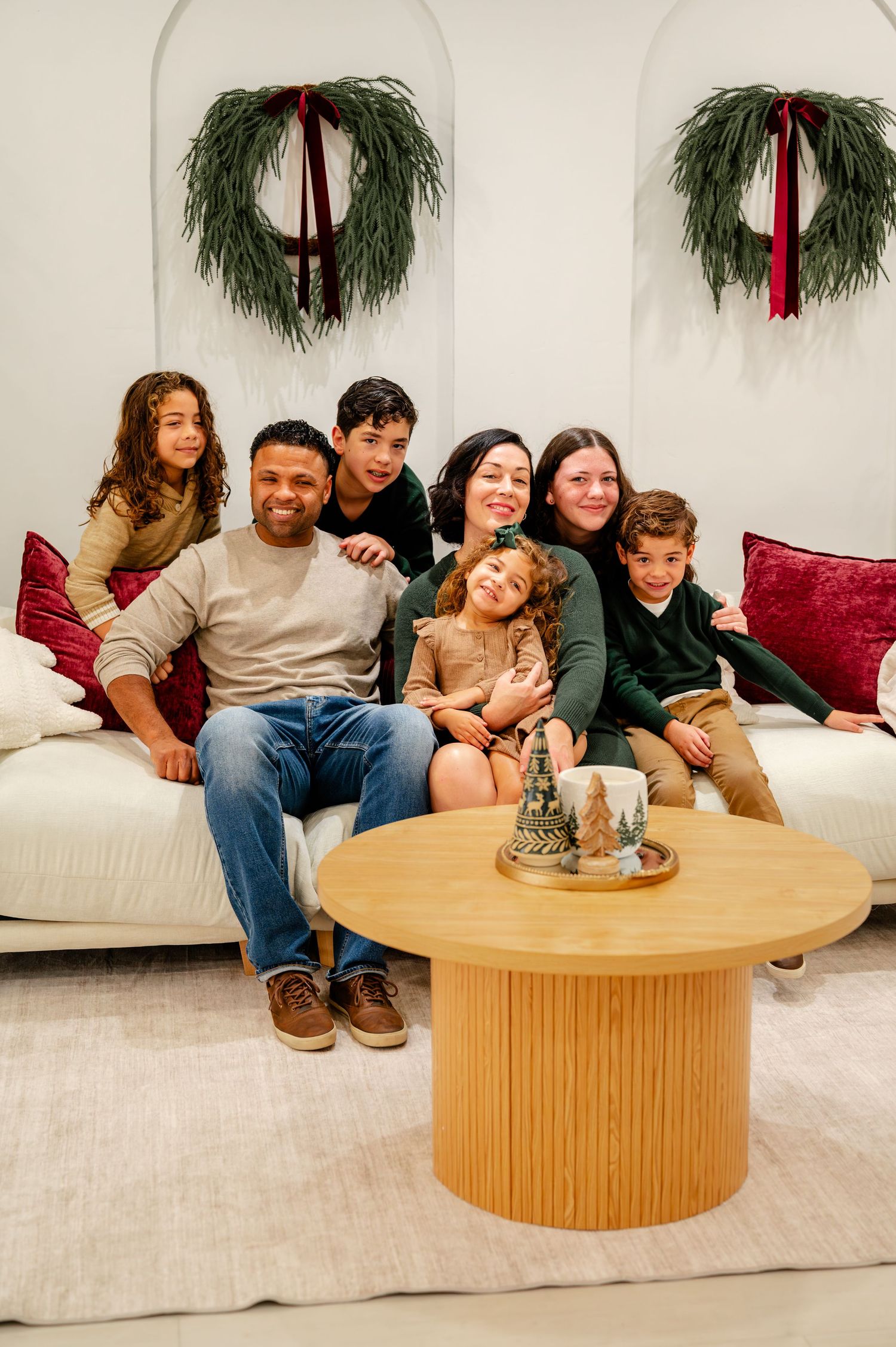 A group sits together on a white couch with evergreen wreaths hanging on the wall behind them during the holidays.