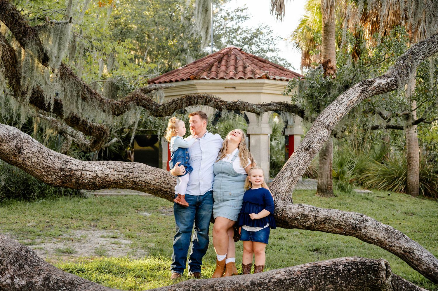 A family enjoys quality time together under sprawling oak trees draped with Spanish moss at a at a spring mini session in jacksonville, fl.