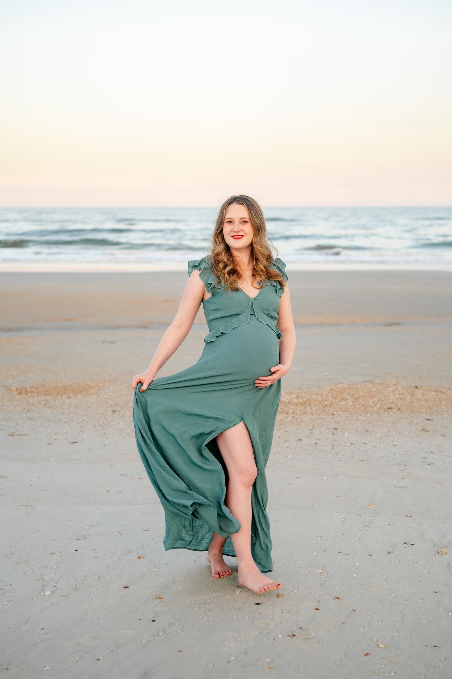 A person in a flowing green dress twirls playfully on a sandy beach at sunset.
