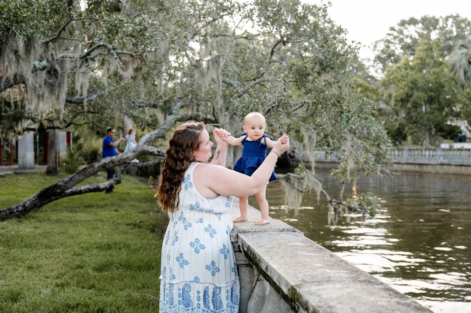 A mom and baby share an intimate moment during a fall mini session in Jacksonville, FL with moss-draped trees and water in the background.