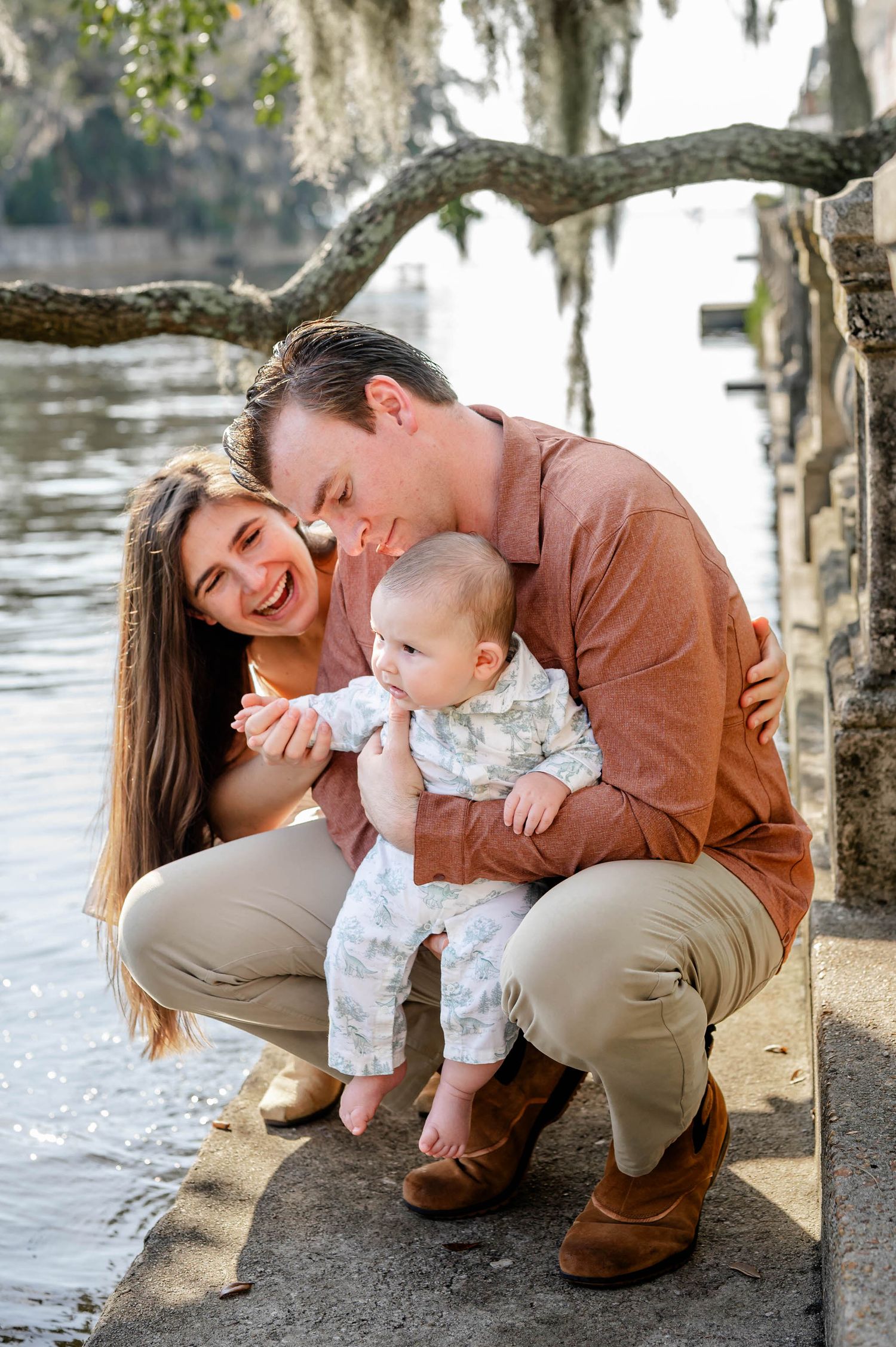 A tender family moment captured outdoors near a lake with Spanish moss hanging from trees at a spring mini session in jacksonville, fl