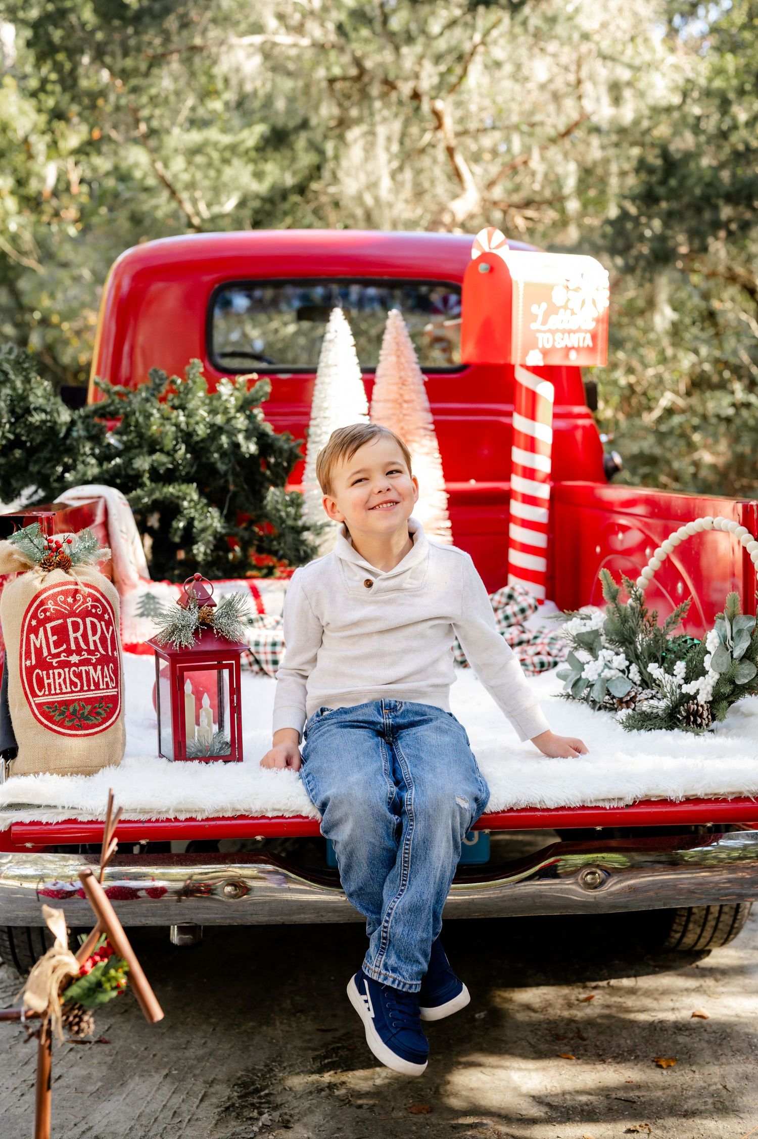 A vintage red pickup truck decorated for Christmas with snow and holiday props in a rustic outdoor setting.