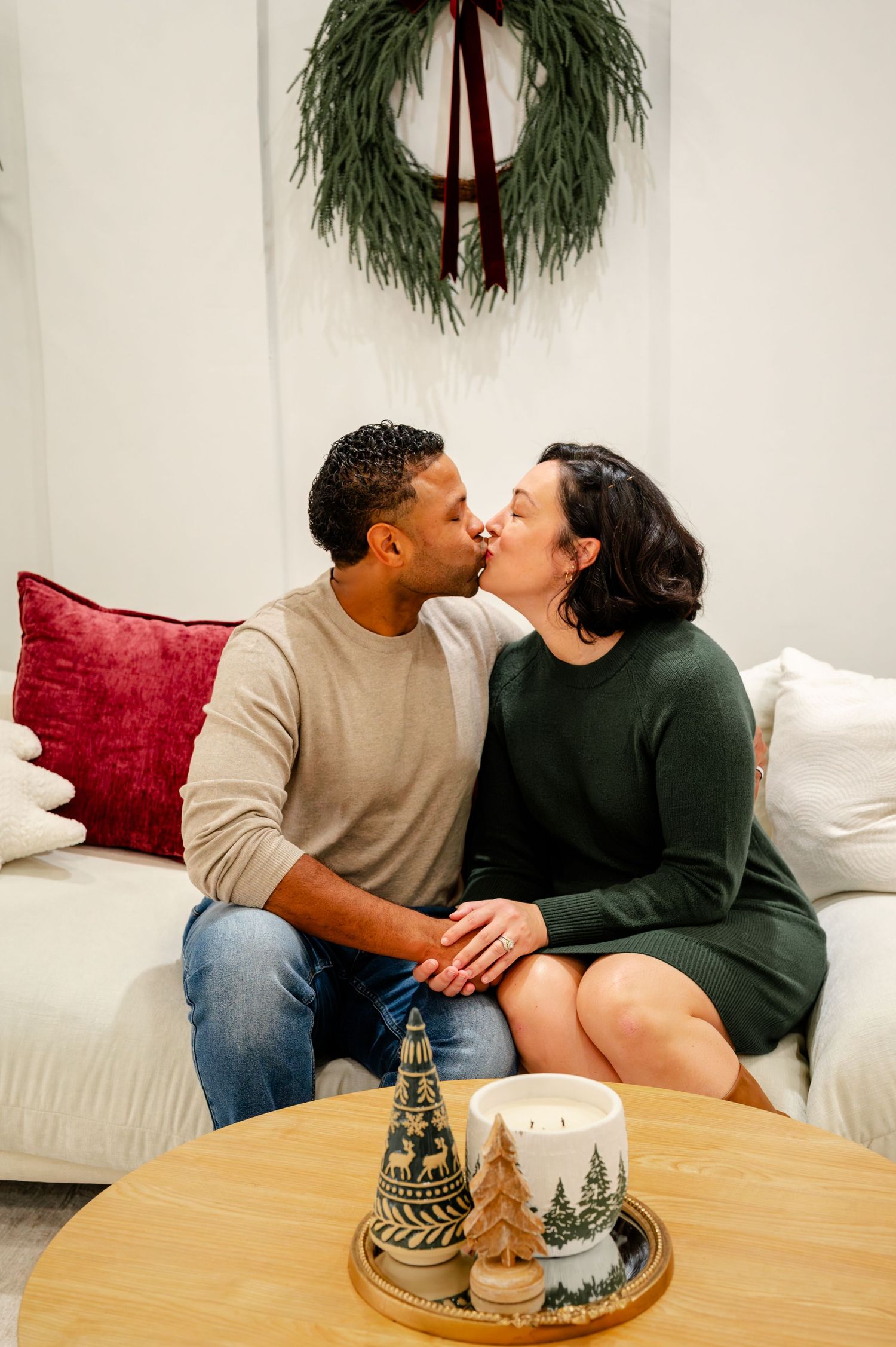 A couple shares a romantic moment on a white couch with holiday decor and winter decorations on the coffee table.
