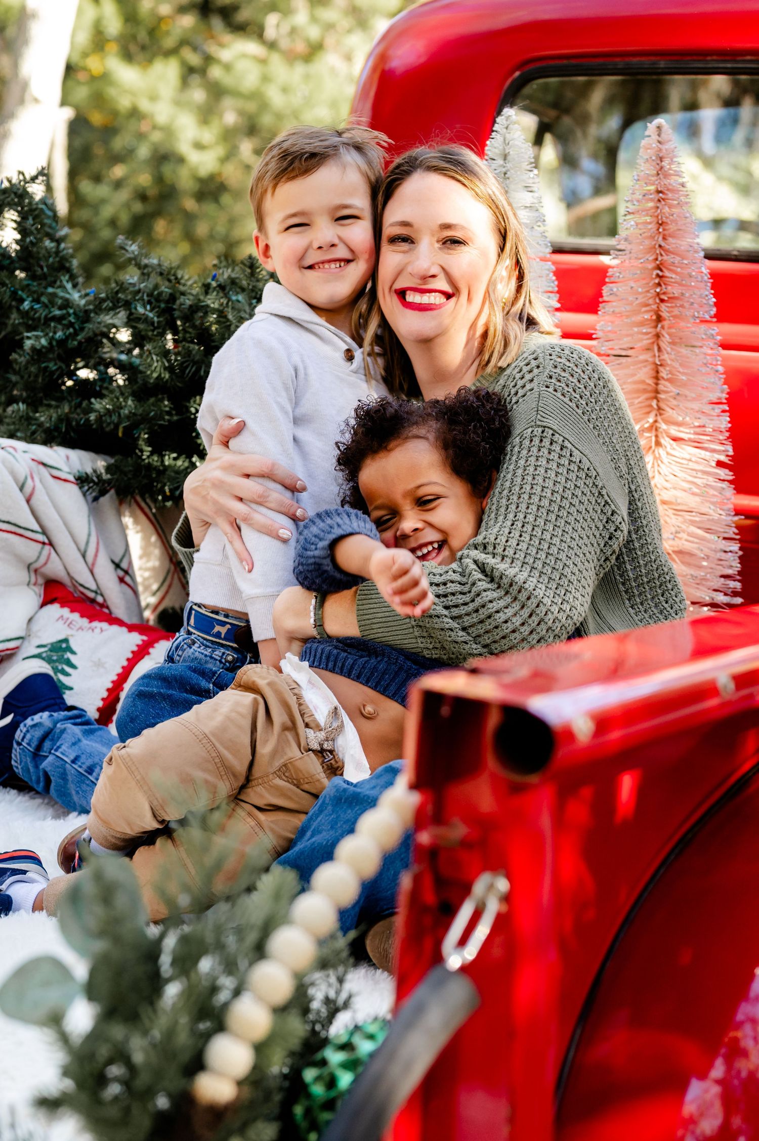 A joyful holiday scene with people laughing together on a bright red vintage truck decorated with Christmas ornaments.