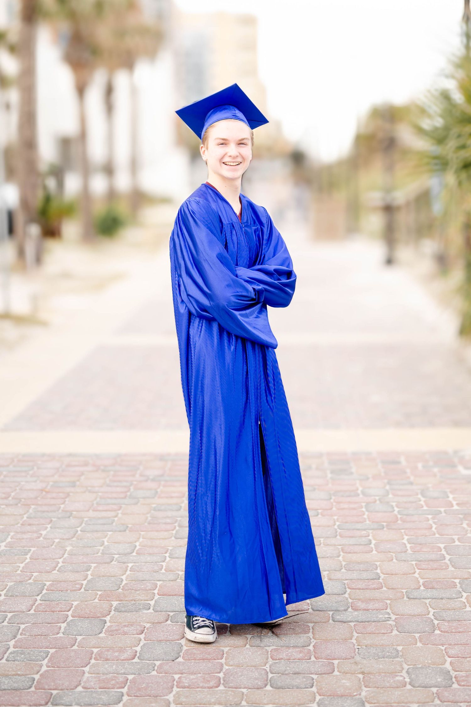 Child in bright royal blue graduation gown poses on brick pathway at various angles outdoors.