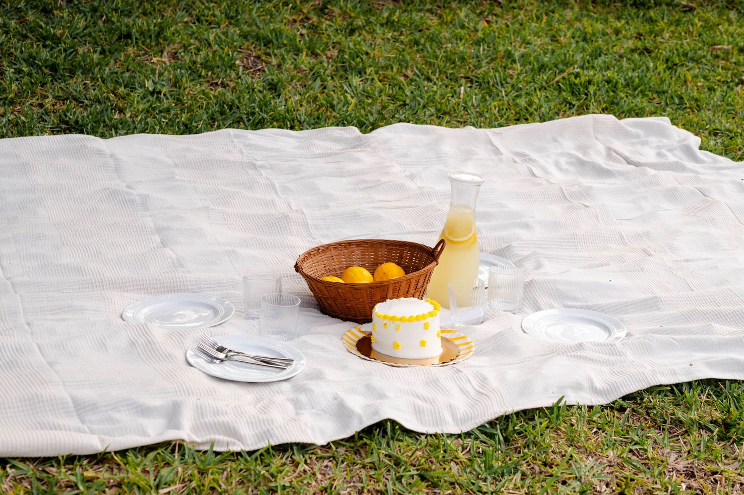 White picnic blanket laid out on grass with wooden bowl and snacks.
