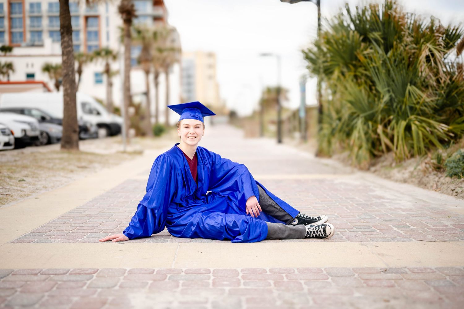 A graduation photo series featuring blue cap and gown poses along a palm tree lined pathway.
