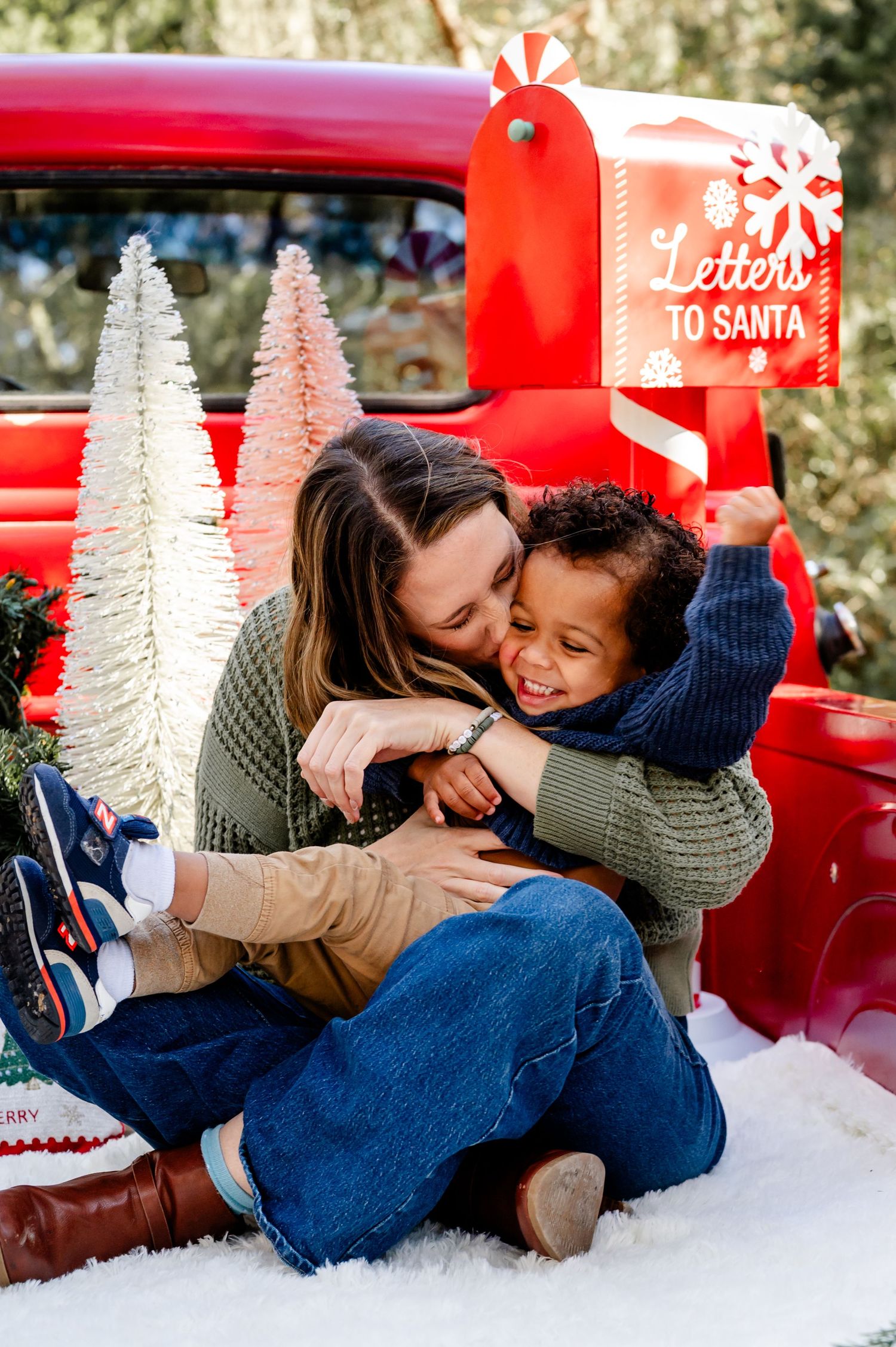 A festive holiday scene with a red vintage truck, white bottle brush trees, and a red Letters to Santa mailbox in the snow.