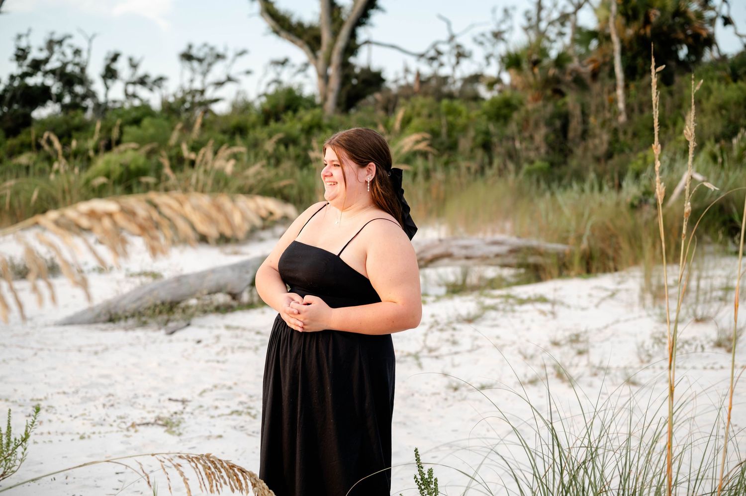 A silhouetted figure walks along a scenic white sand beach trail with dune grass and trees at dusk.