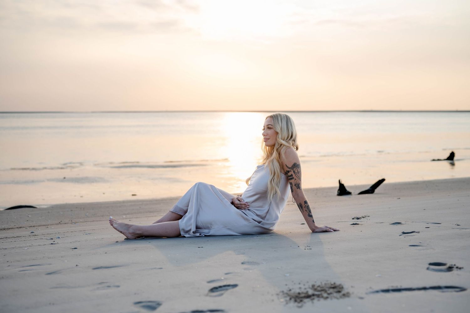 Maternity photo of woman in satin dress sitting on beach at sunrise on Black Rock Beach, Jacksonville.