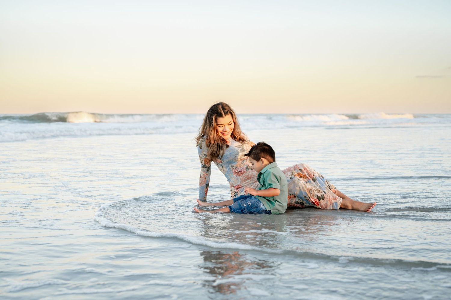 Two people playing and splashing in the ocean waves at sunset on a beach.