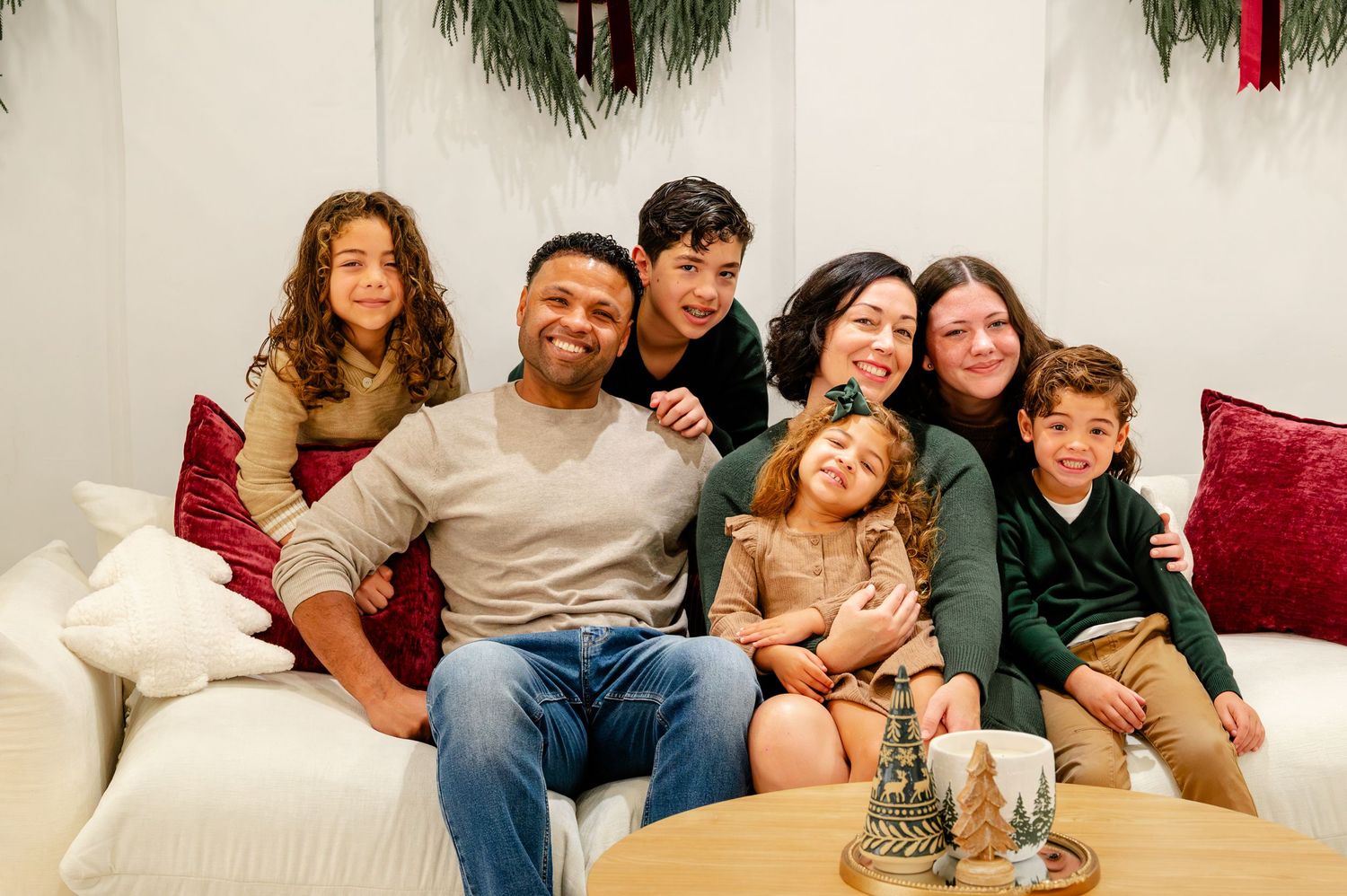 A family sits together on a white couch with holiday decorations visible in the background.