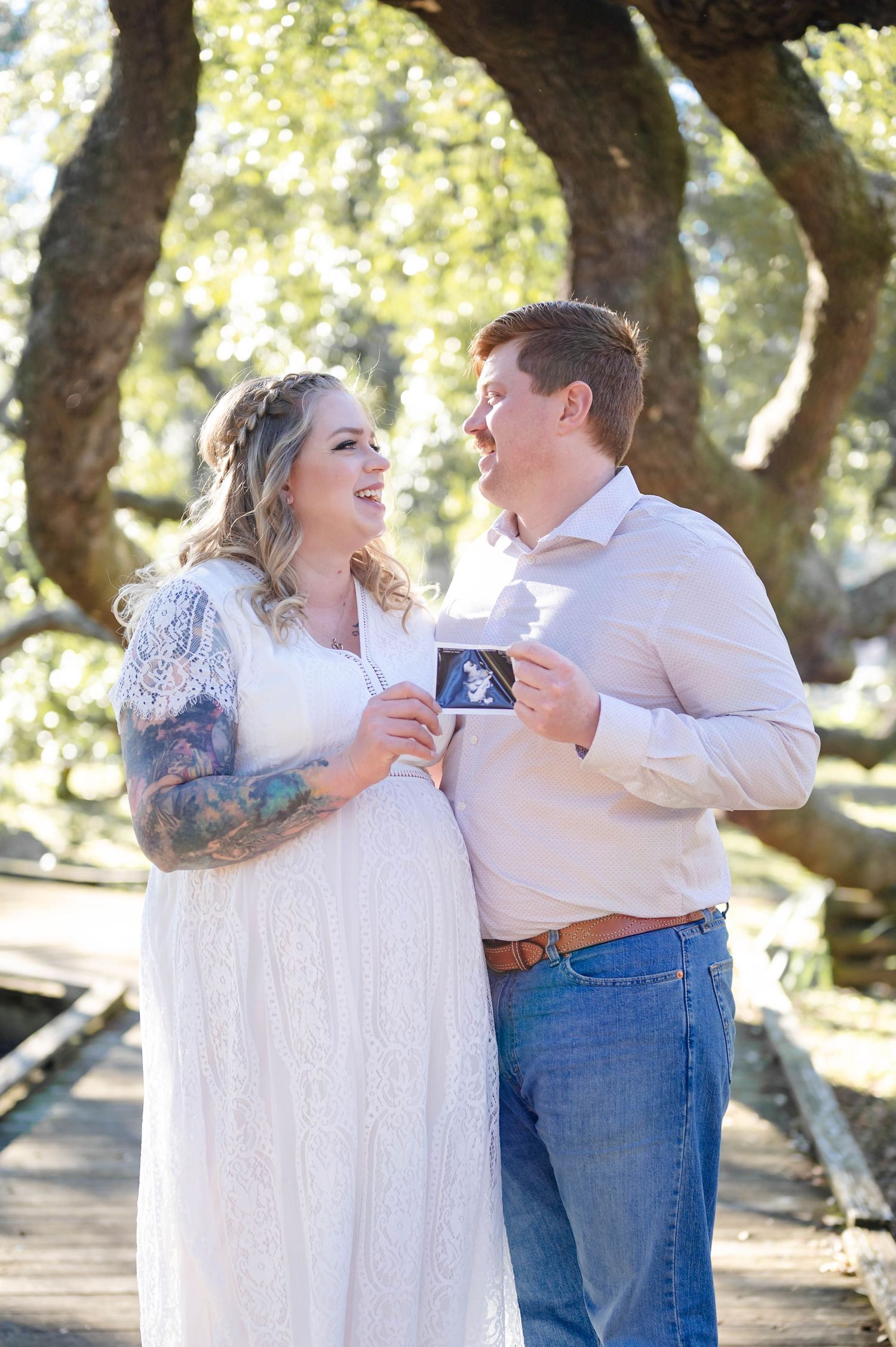 Couple shares romantic moment while holding sonogram photos in outdoor setting.