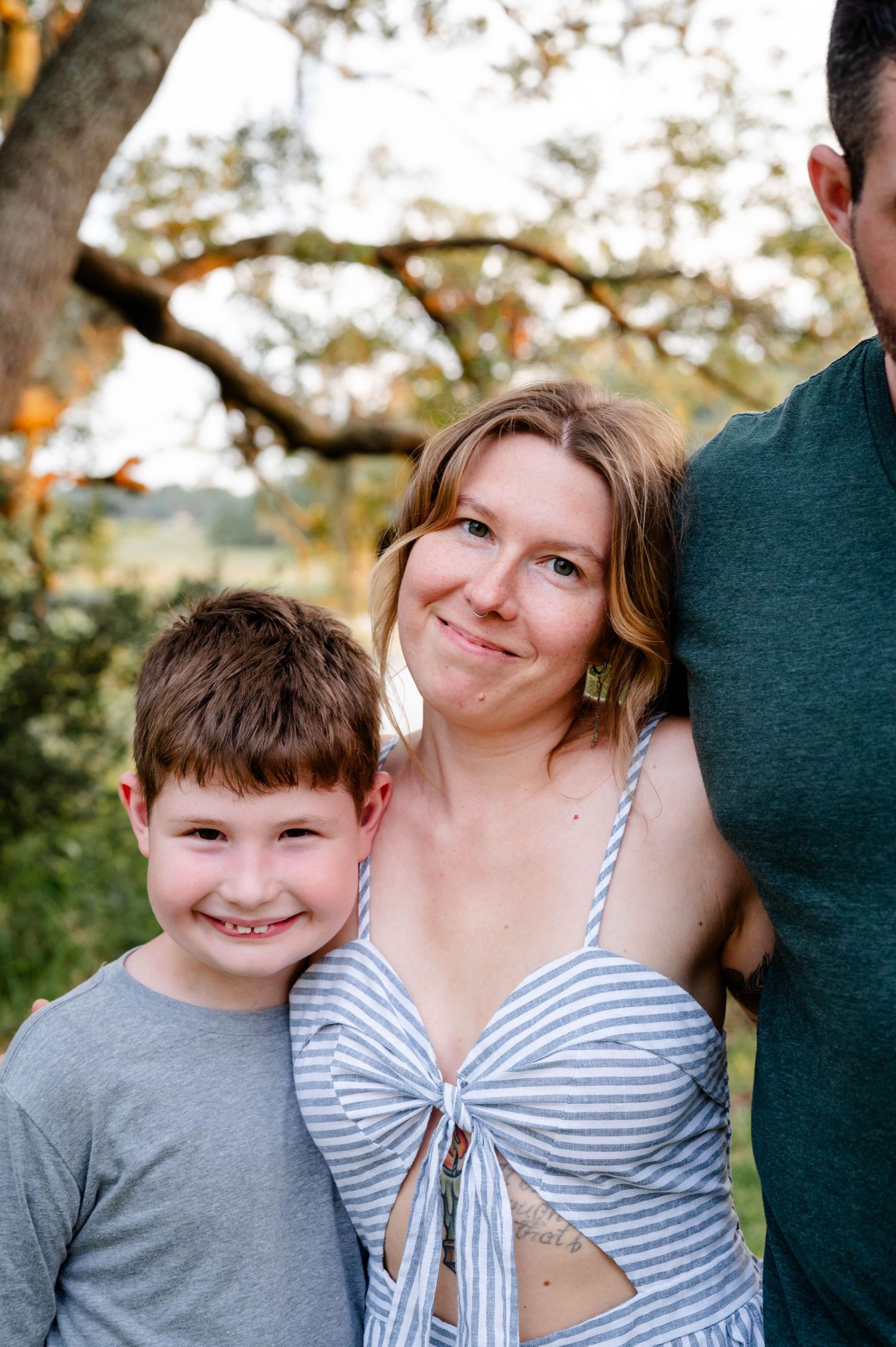 A casual outdoor family photoshoot with people wearing grey and striped clothing against a natural backdrop in a Jacksonville park.